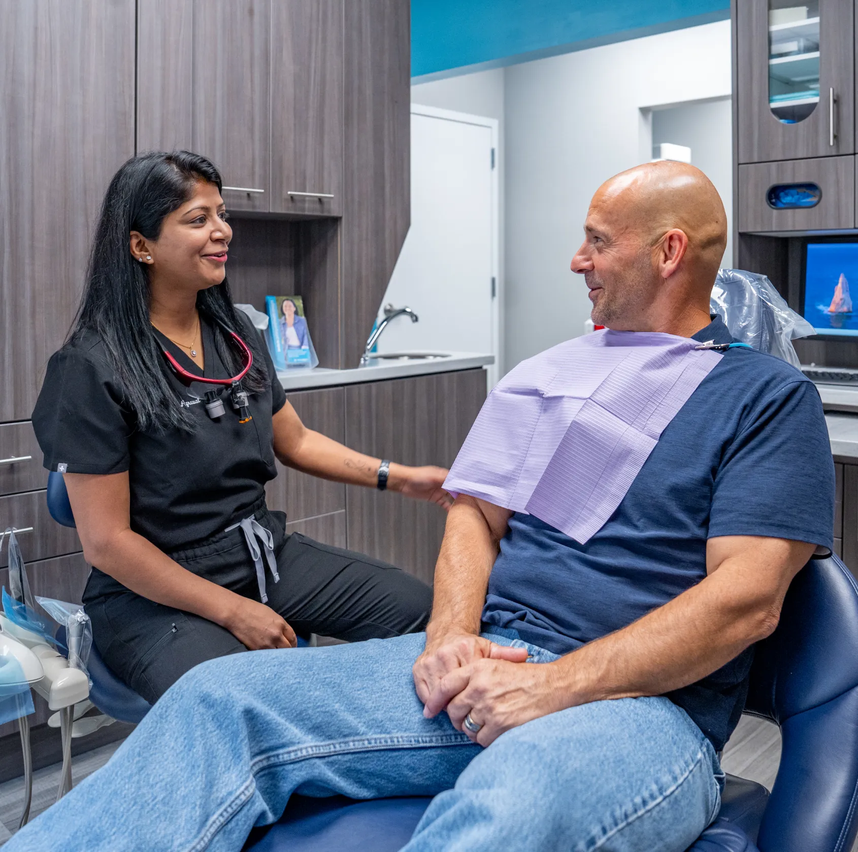 Dentist talking to a smiling patient sitting in a dental chair.