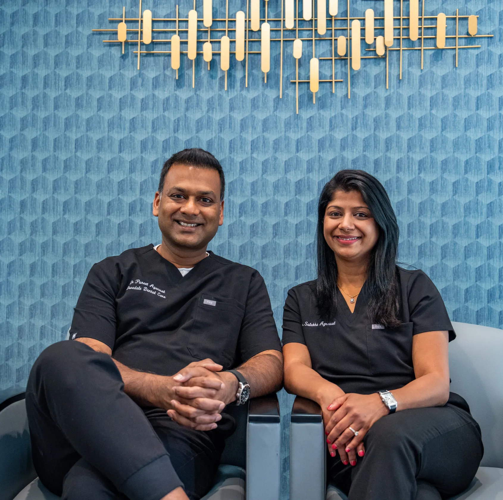 Two smiling people in black uniforms sit on a couch in a modern office setting.