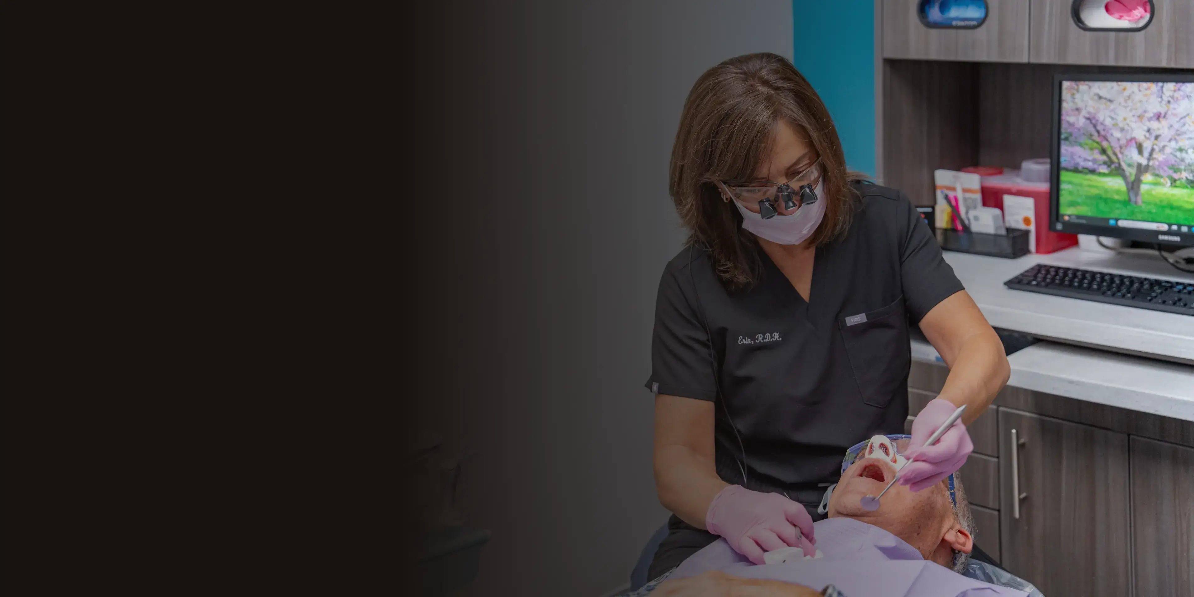 A dental professional wearing a mask examines a patient's teeth in a dental office.