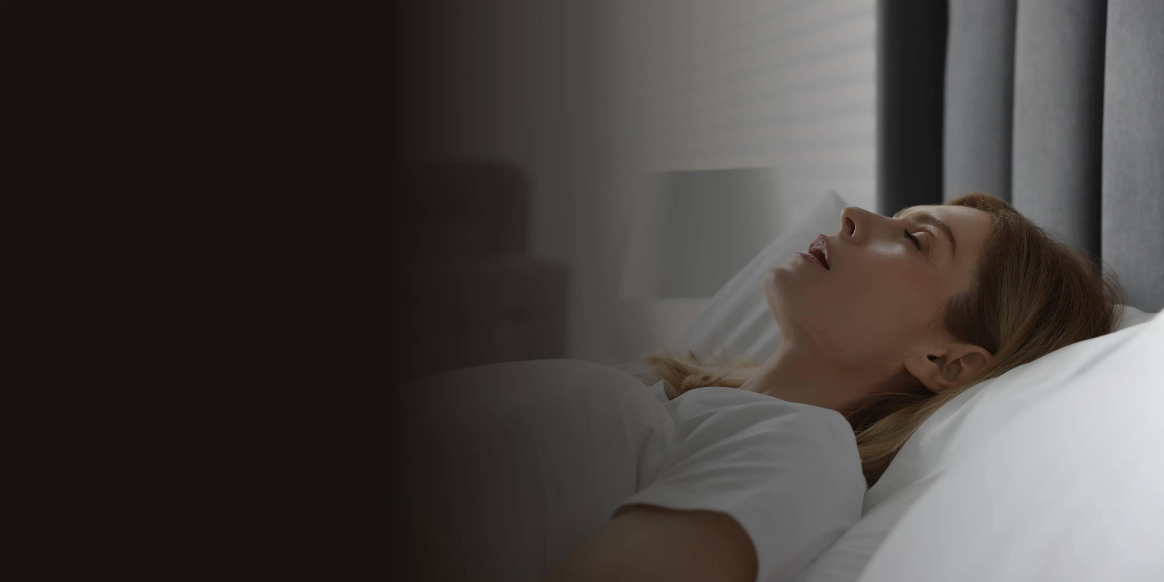 A woman lies on a bed, staring upward, in a dimly lit room.