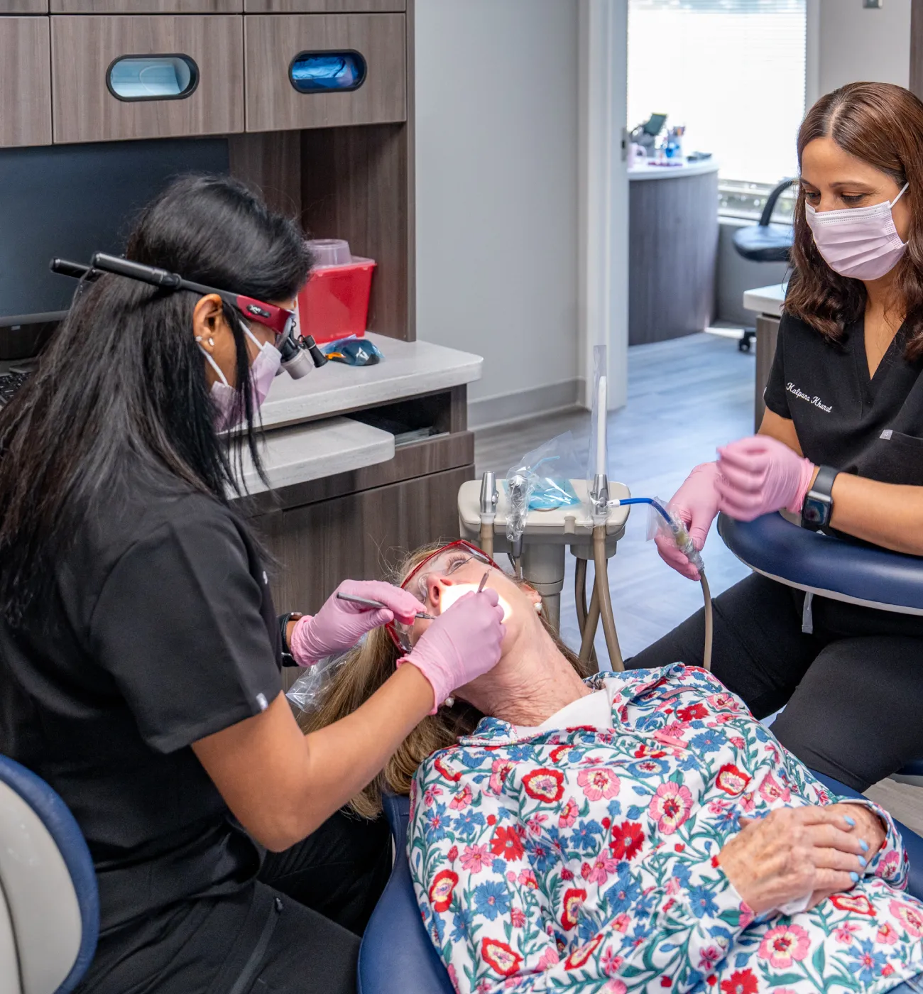 Two dental professionals work on a patient lying in a dental chair, wearing protective masks and gloves.