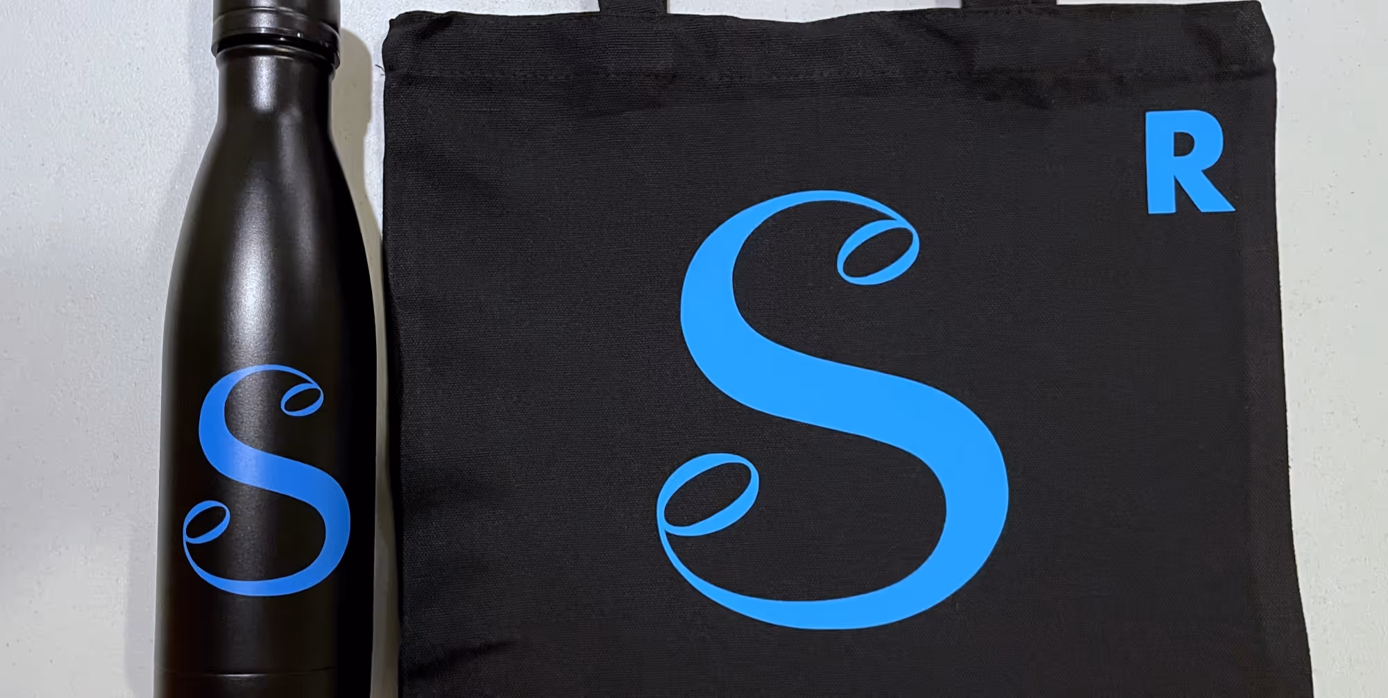 Black waterbottle and bag with blue "S" logo and smaller "R" initial