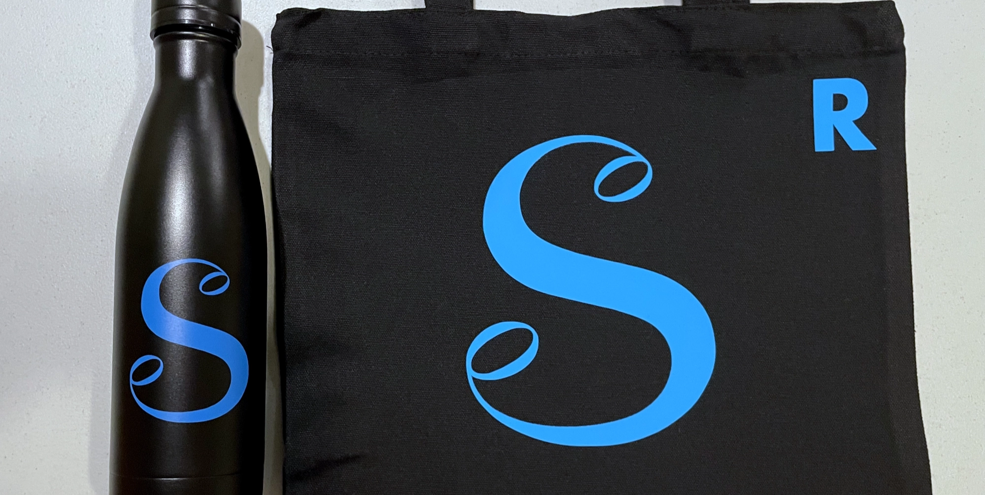 Black waterbottle and bag with blue "S" logo and smaller "R" initial