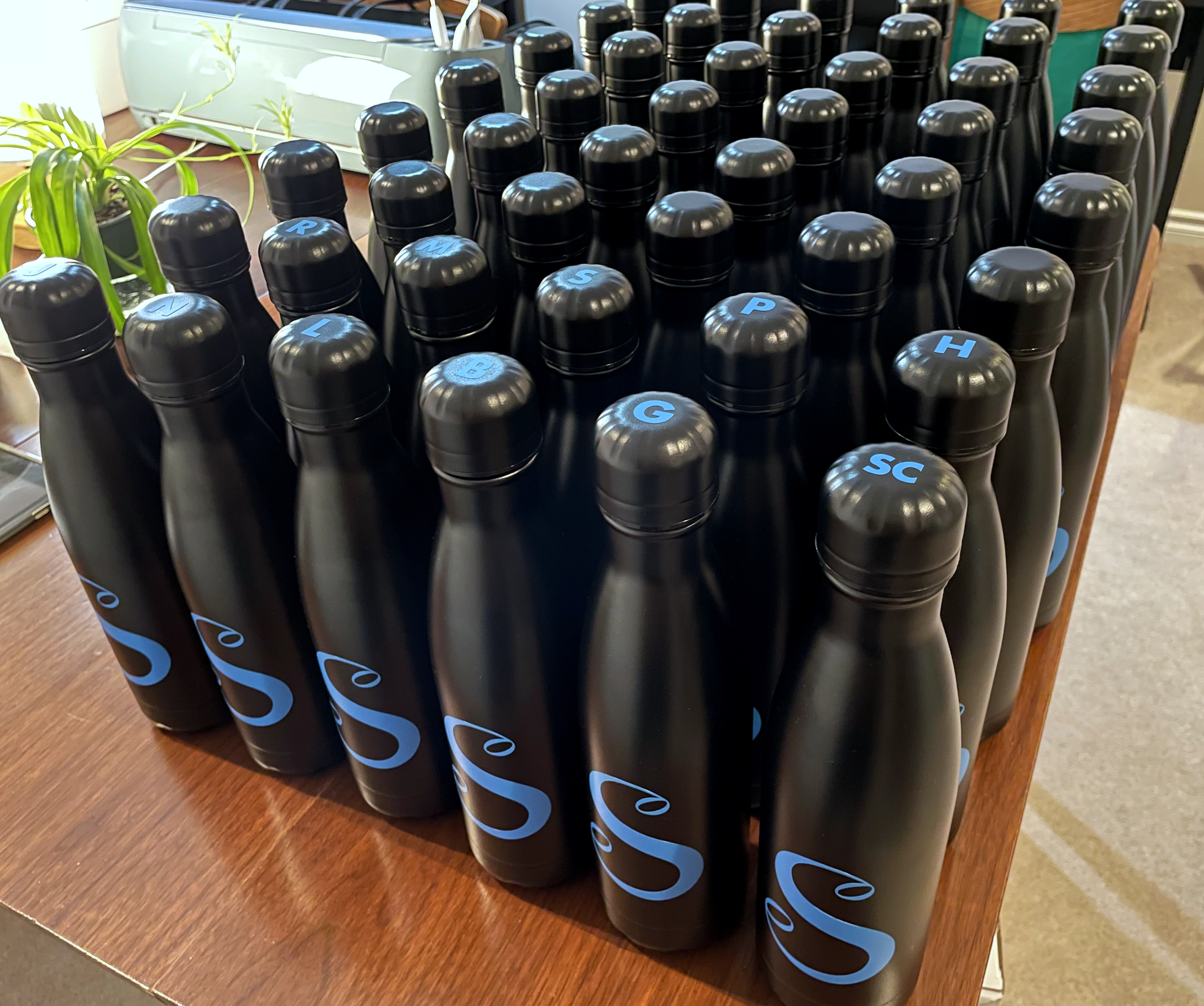 50 water bottles with 'S' logo on bottle, some with initials on the lids
