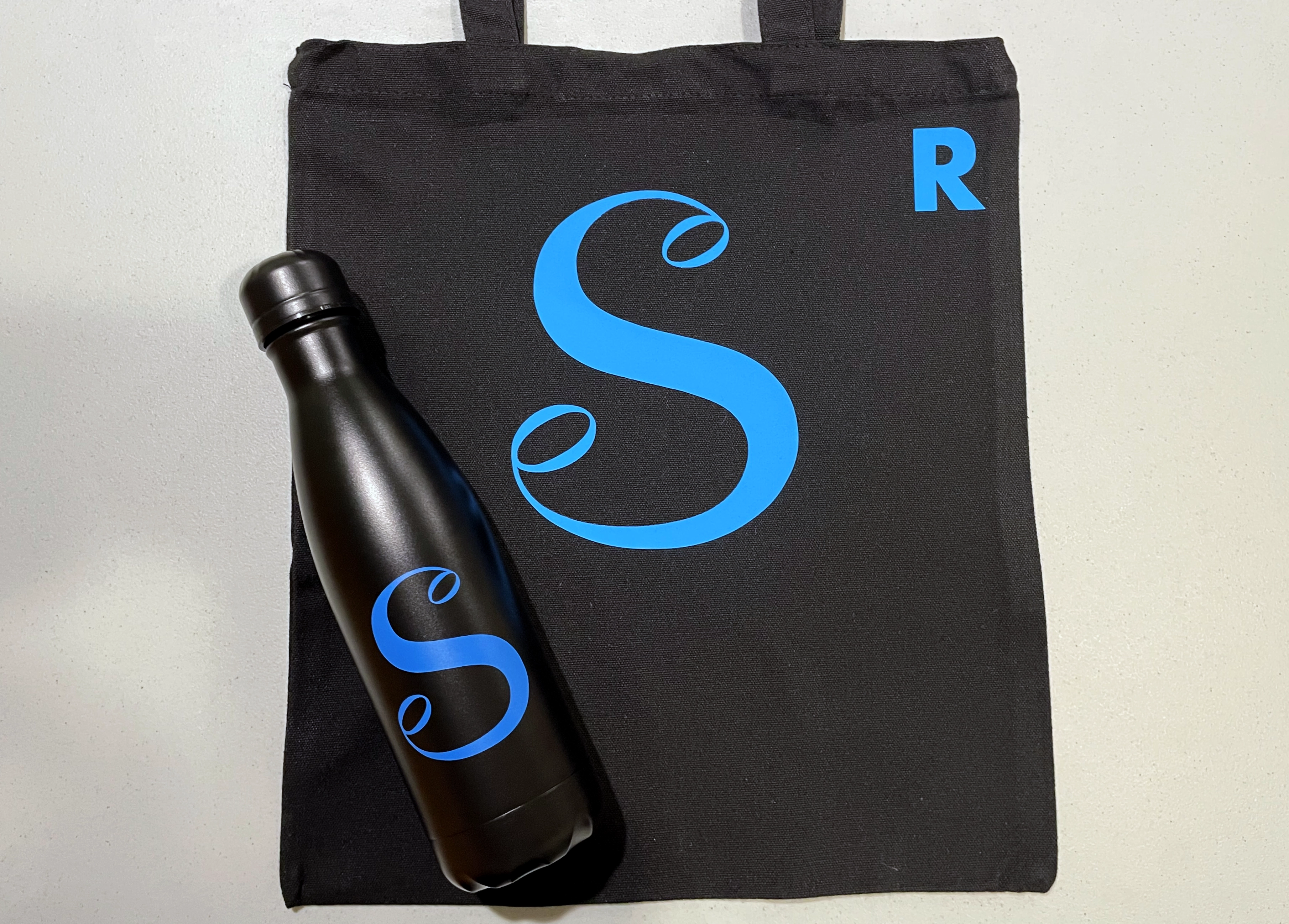 Black waterbottle and bag with blue "S" logo and smaller "R" initial