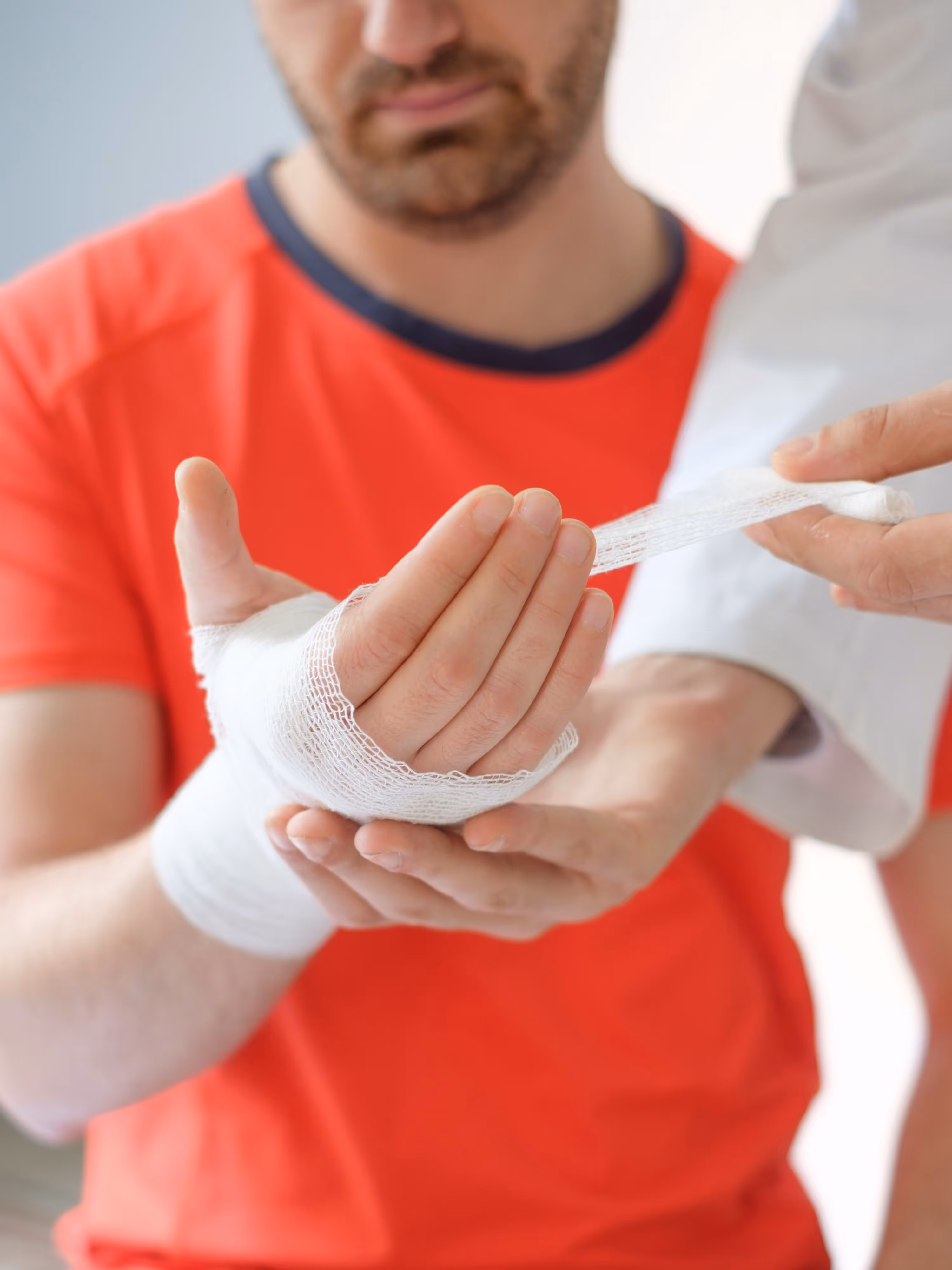 A man in an orange shirt holding a bandaged hand.