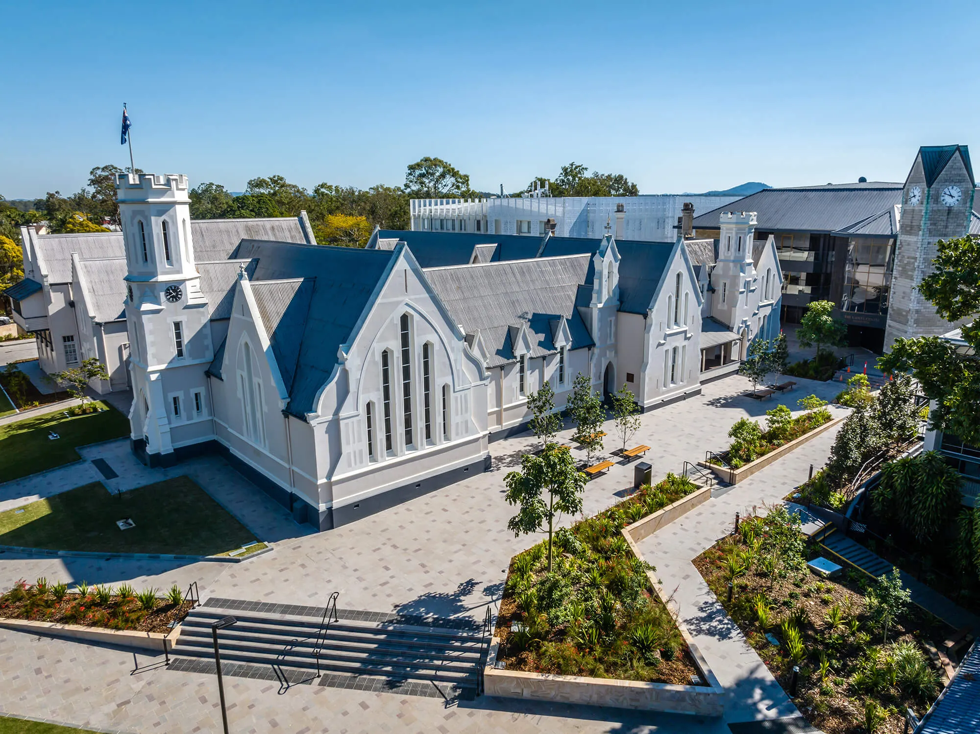 Aerial view of a large historic white building with pointed roofs and clock towers surrounded by landscaped gardens and pathways.