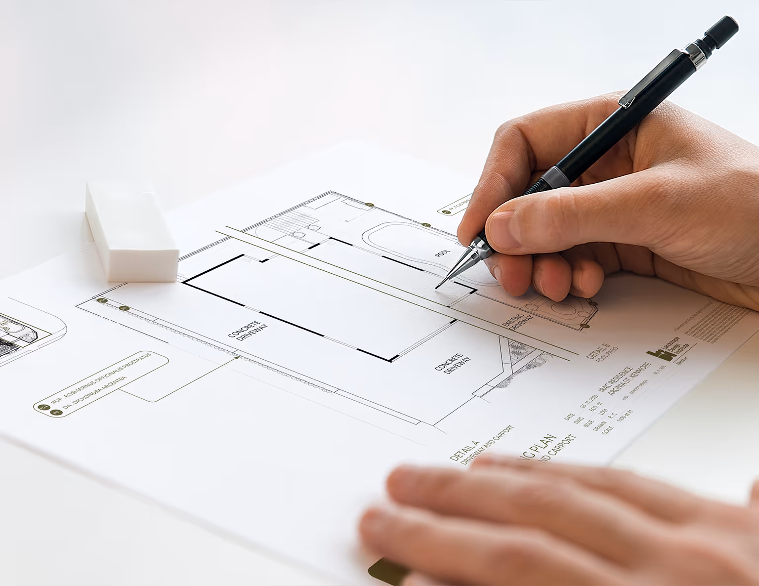 Close-up of a hand drawing on architectural blueprint with a mechanical pencil and an eraser nearby.
