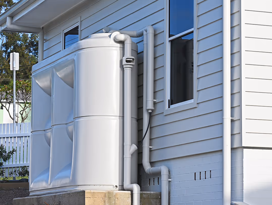 Large white rainwater tank connected to a house gutter system for water collection and storage.