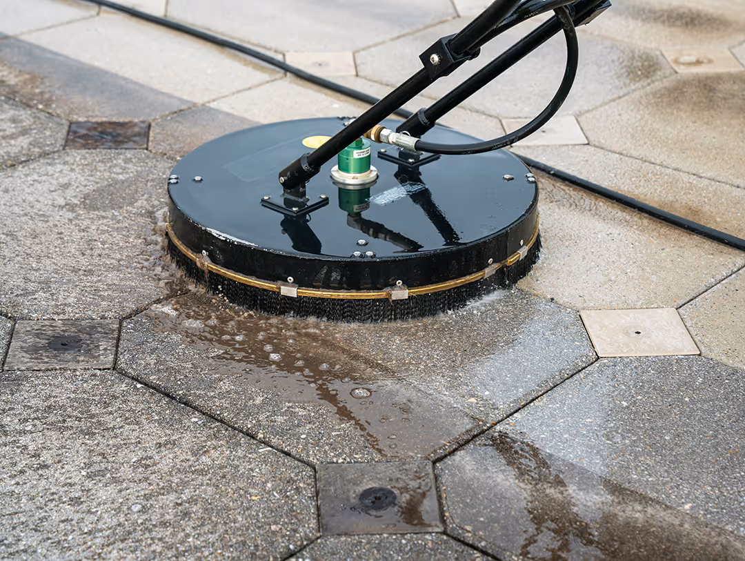 Surface cleaner pressure washing hexagonal concrete pavement, showing wet and clean areas.