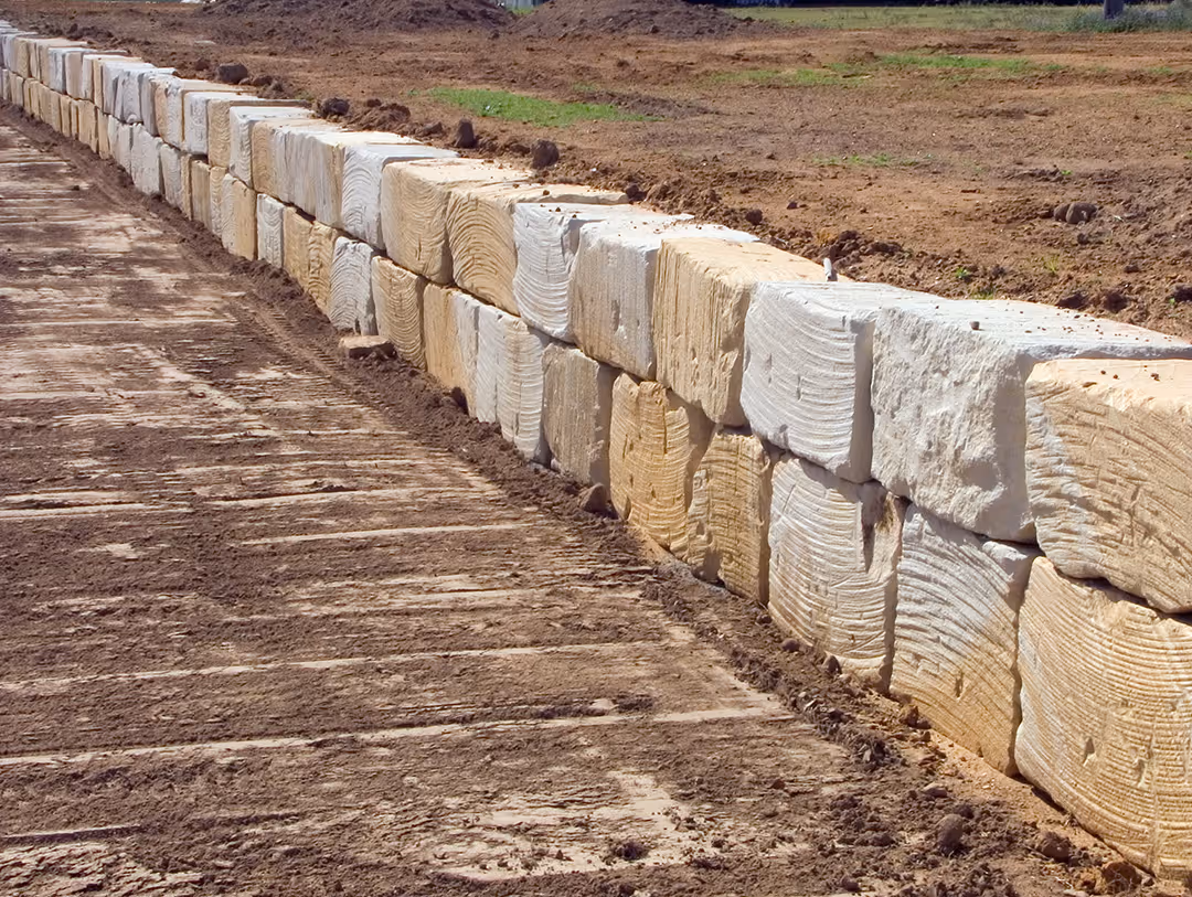 Retaining wall made of large, textured stone blocks on a cleared, dirt surface.