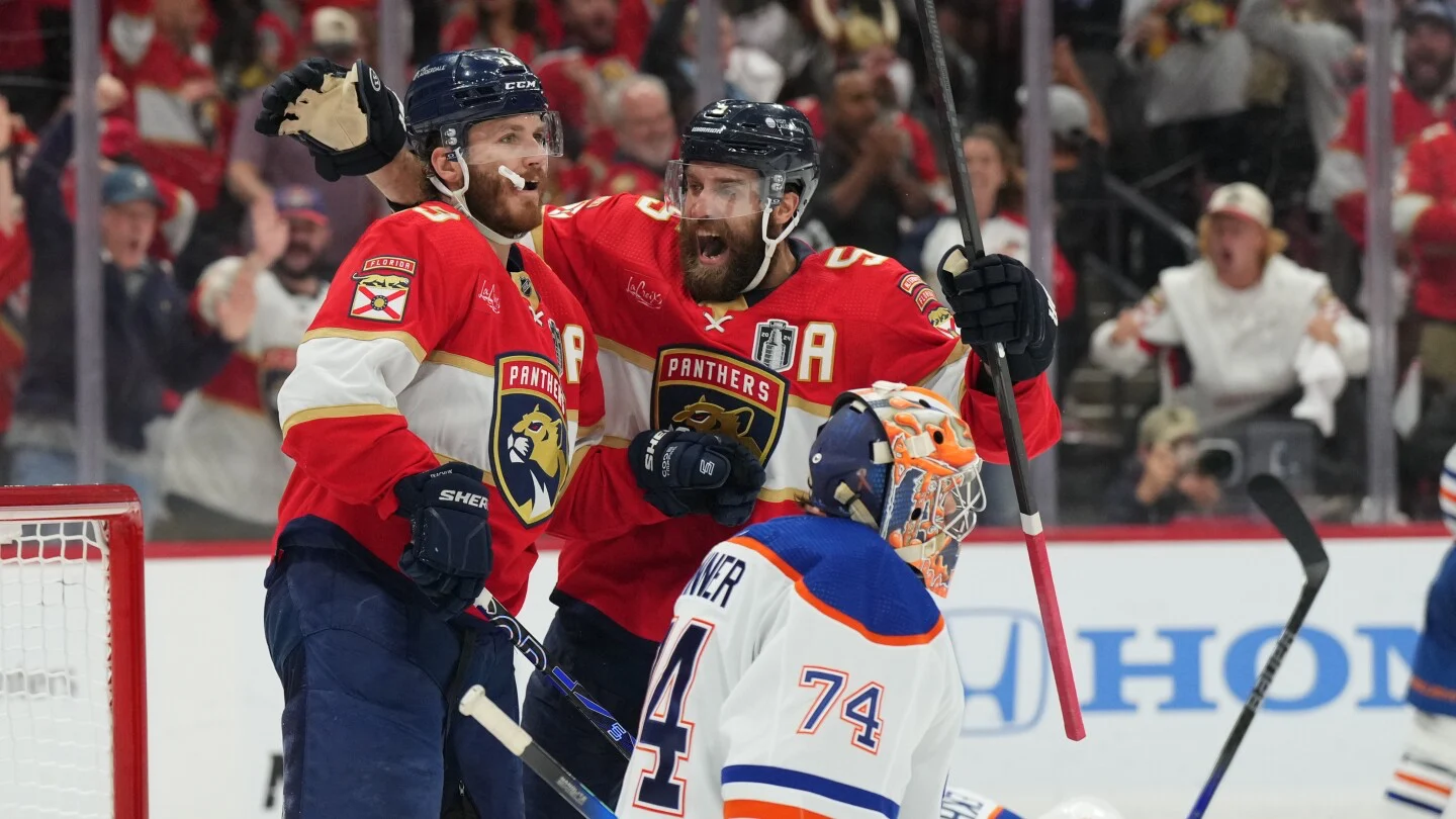 Florida Panthers hockey players celebrate a goal against the Edmonton Oilers during an NHL game, with fans cheering in the background and Oilers goalie Stuart Skinner looking on.