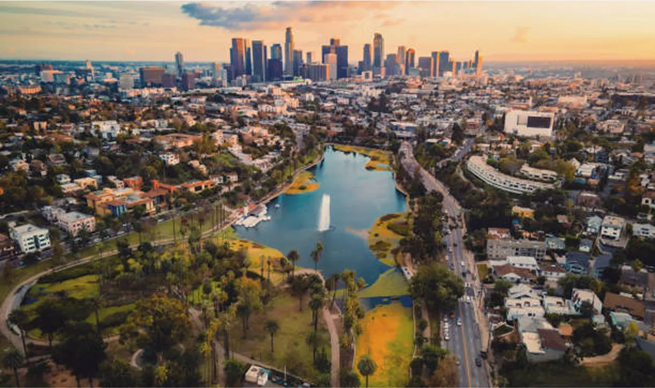 Aerial view of Los Angeles, California at sunset, showcasing the downtown skyline, Echo Park Lake with a fountain, and surrounding residential neighborhoods.