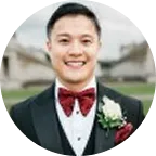 Michael Dinh-Ho, founder of MDH Properties, smiling in formal attire with a red bow tie and boutonnière, posing outdoors.