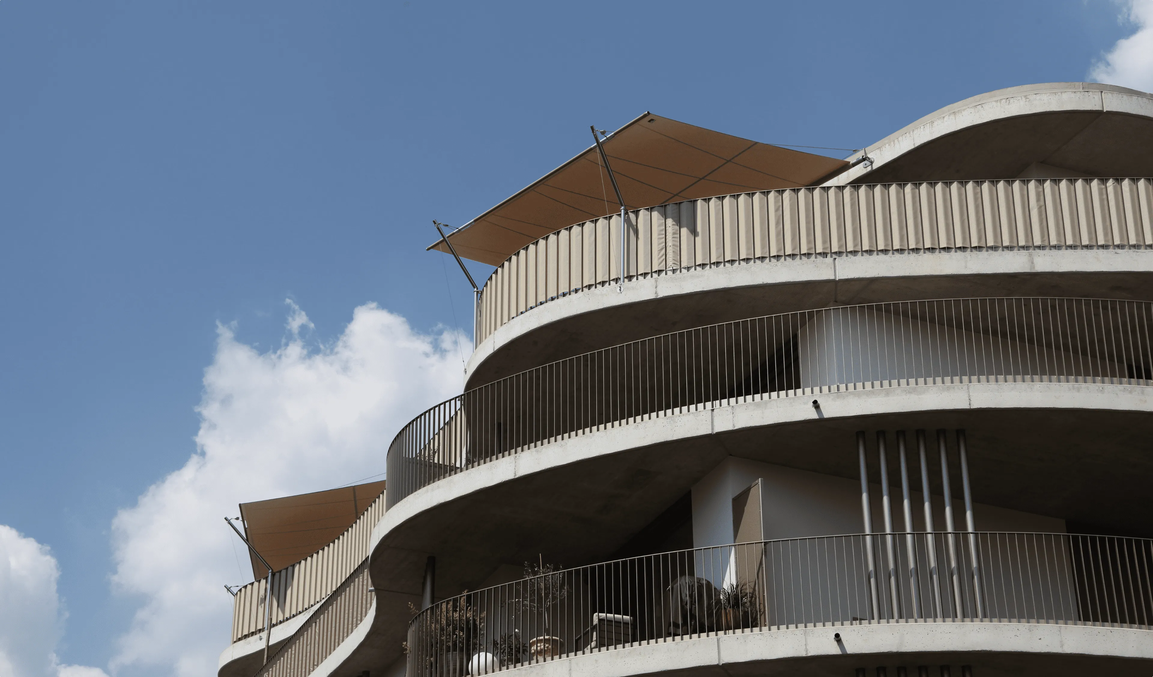 Architekturwohnhaus mit geschwungener Fassade zeigt zwei einseitige Rechtecksegel, die den Balkon im obersten Geschoss mit Schatten versehen.