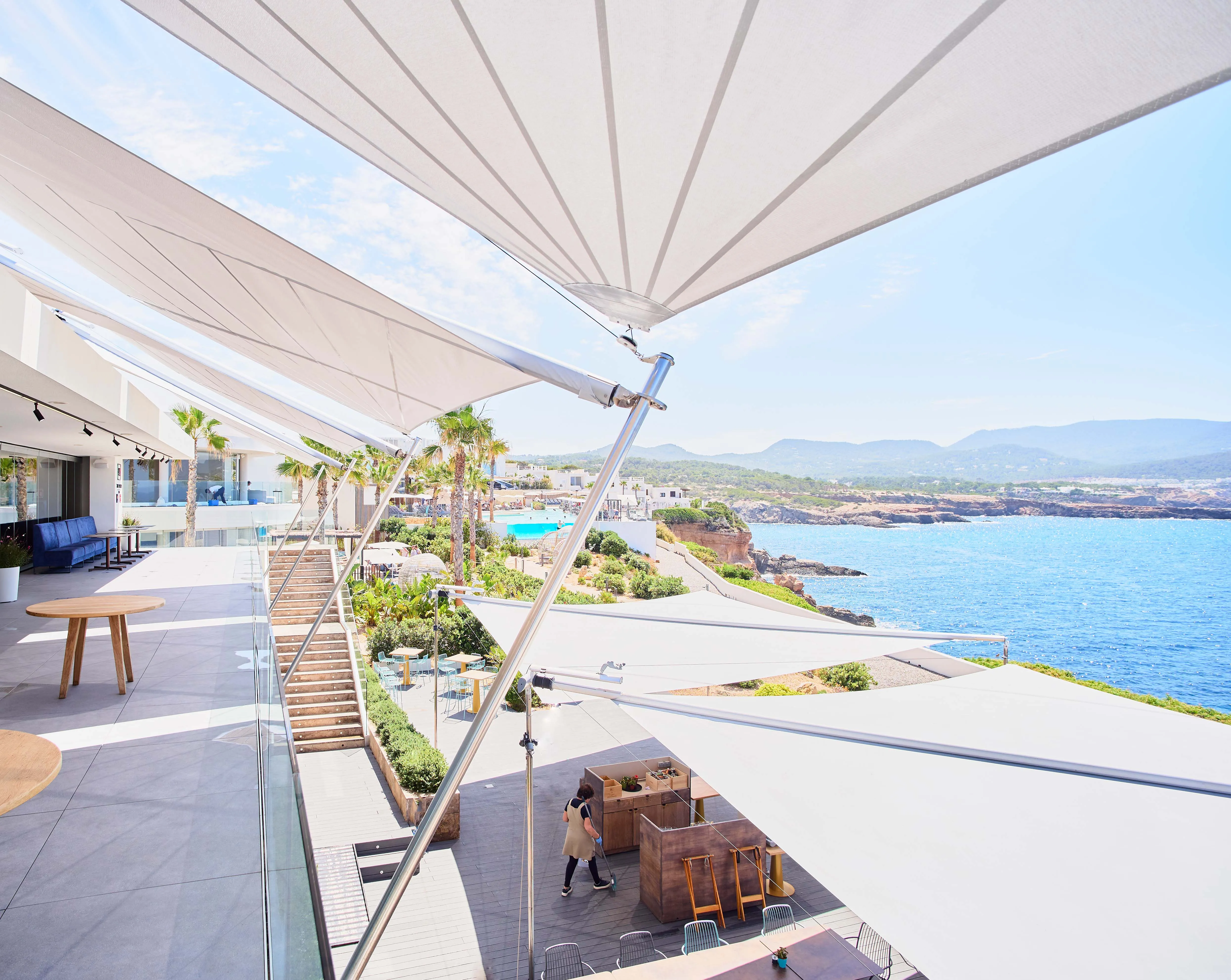 Ein Projekt der ästhetischen Superlative. Sieben SunSquare SQK-Anlagen wurden im 7Pines Resort auf Ibiza in Betrieb genommen. Gezielt wurden die Terrassenbereiche der Restaurants und Bars vor Sonne geschützt. Die eleganten Segel schaffen ein angenehmes Mikroklima, das sowohl tagsüber als auch in den Abendstunden für ein komfortables Gästeerlebnis im Freien sorgt.
Die Kombination aus ästhetischem Design, technischer Raffinesse und maßgeschneiderter Integration in die Architektur des Resorts macht dieses Projekt zu einem Vorzeigebeispiel für hochwertige Outdoor-Beschattung in der gehobenen Gastronomie.
Die Umsetzung erfolgte durch den erfahrenen SunSquare Partner Incompar Balear.