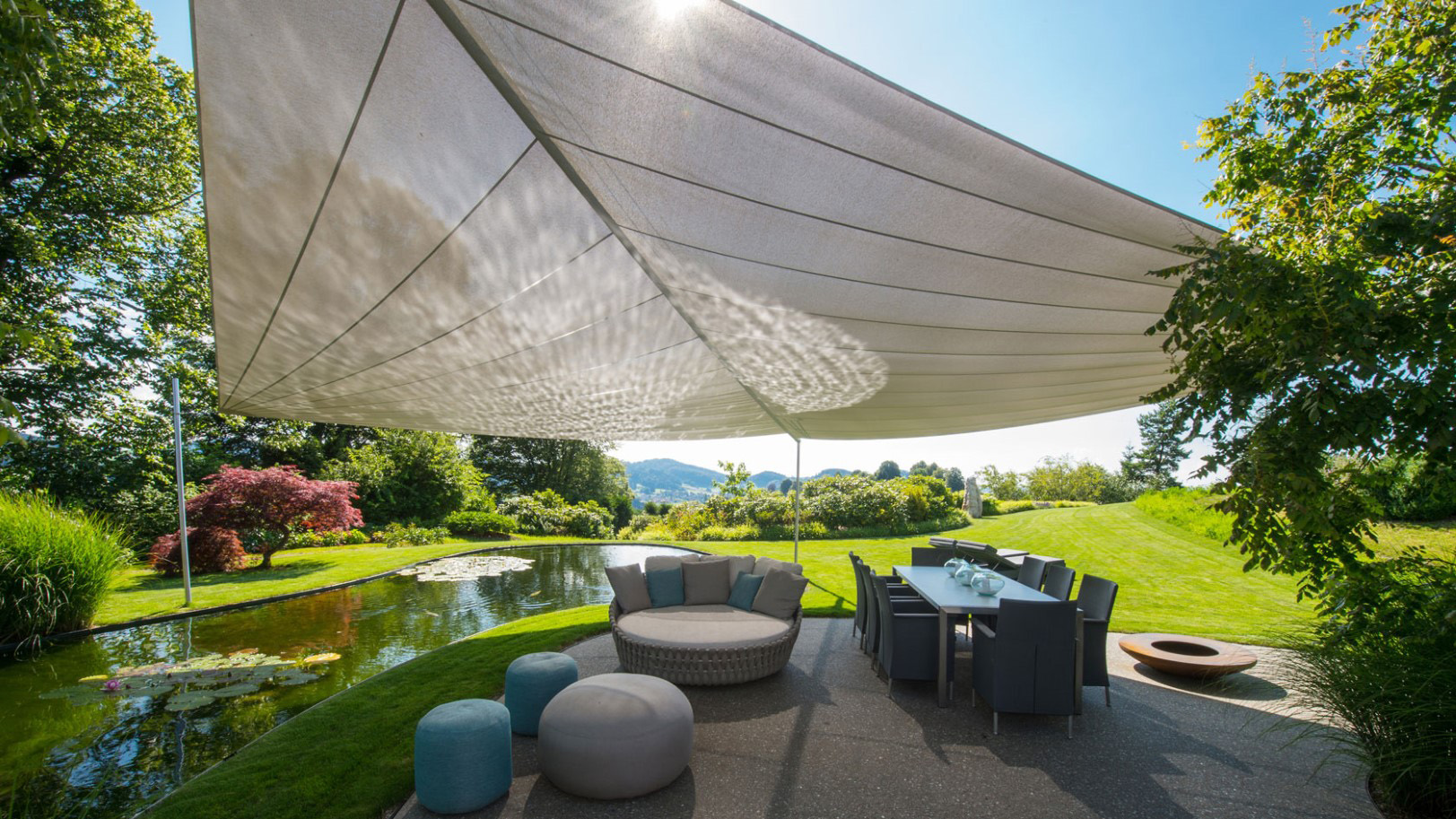 A triangular SunSquare sun sail provides shade for a dining area and the adjacent swimming pool.