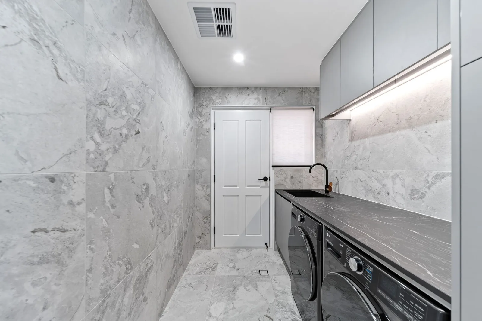 Renovated laundry with dark benchtop and marble-look tiles in a Craigburn Farm home