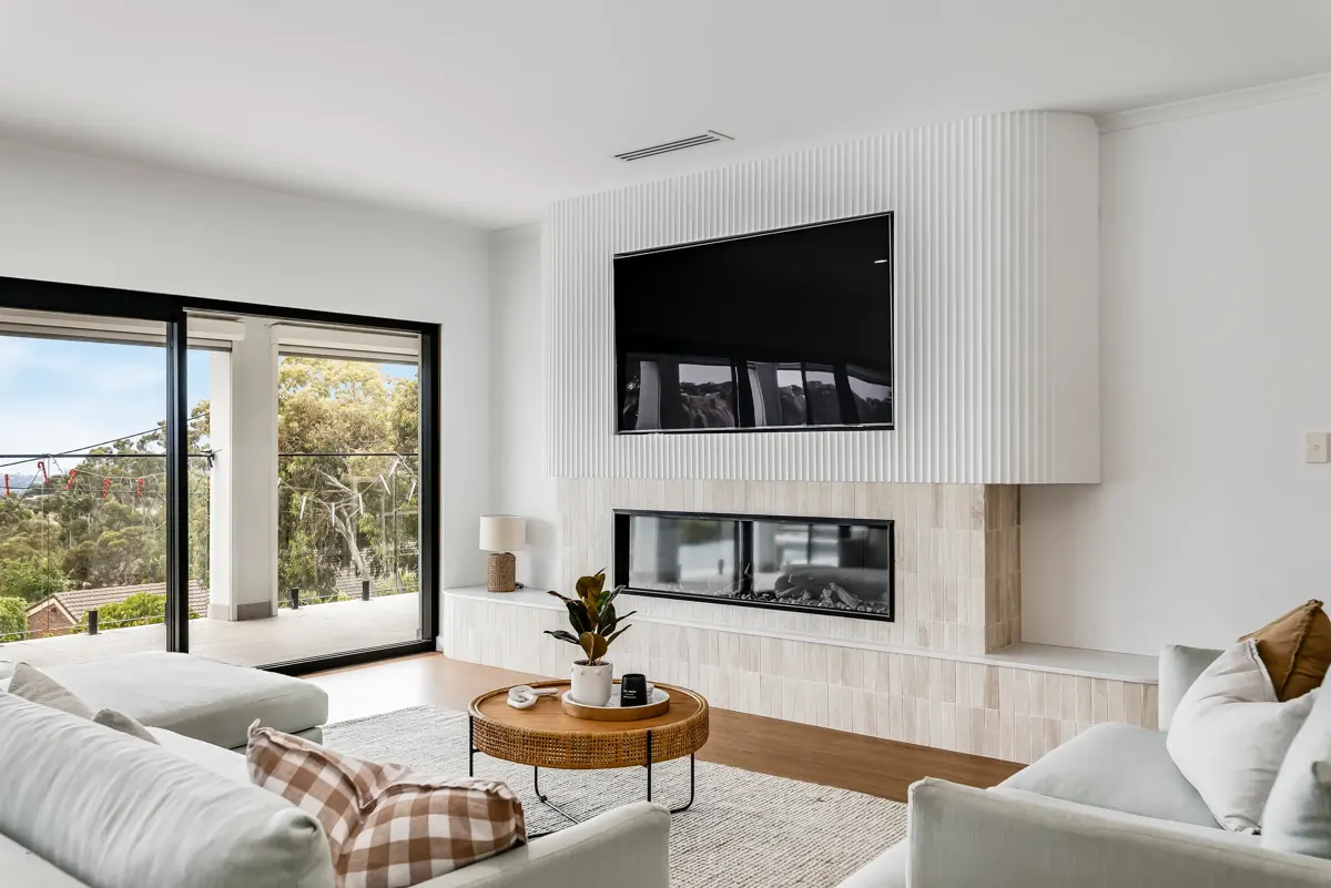 Living room with a fireplace and fluted feature wall beside glass doors to a treed view, Jennifer Ave, Bellevue Heights