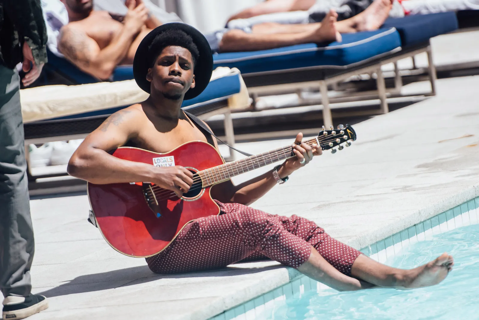 Person playing acoustic guitar at an outdoor pool.