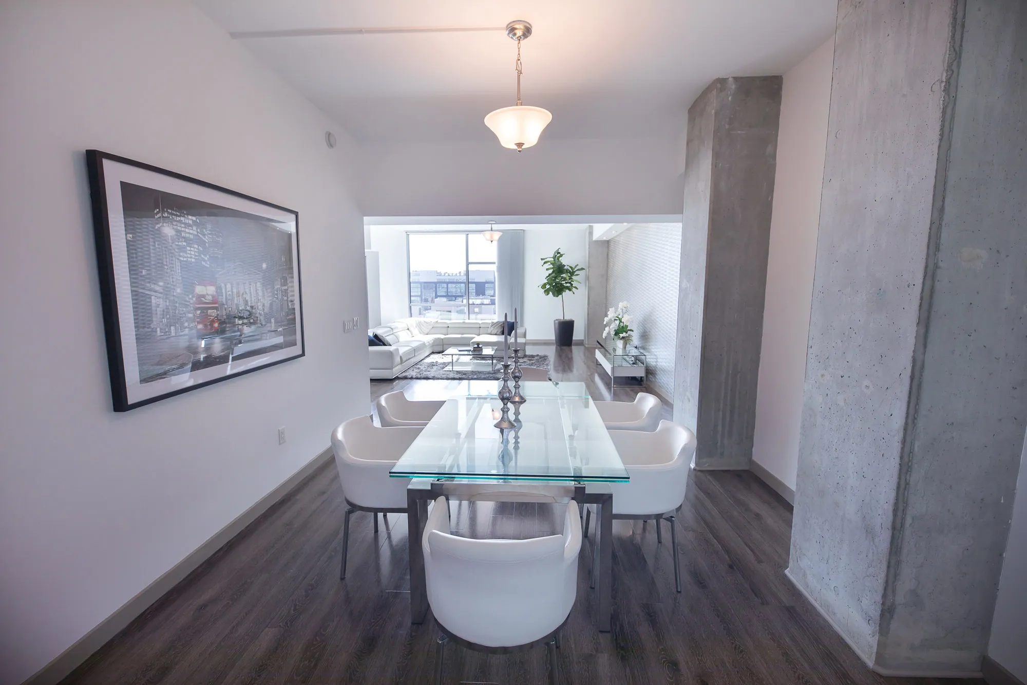 Small glass dining table surrounded by a large painting and grey pillars on either wall.