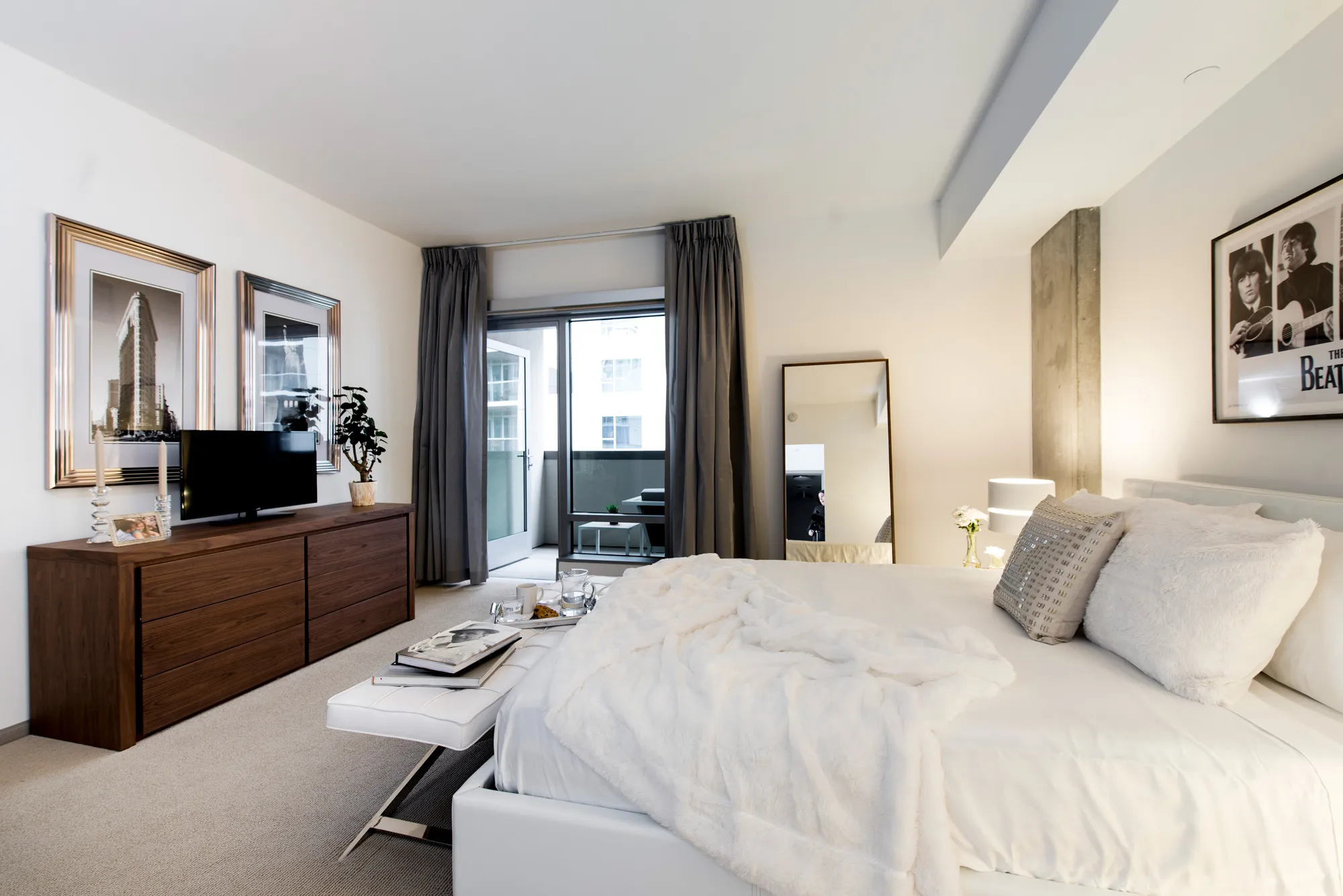 Light apartment bedroom with brown window curtains opening up to small porch.