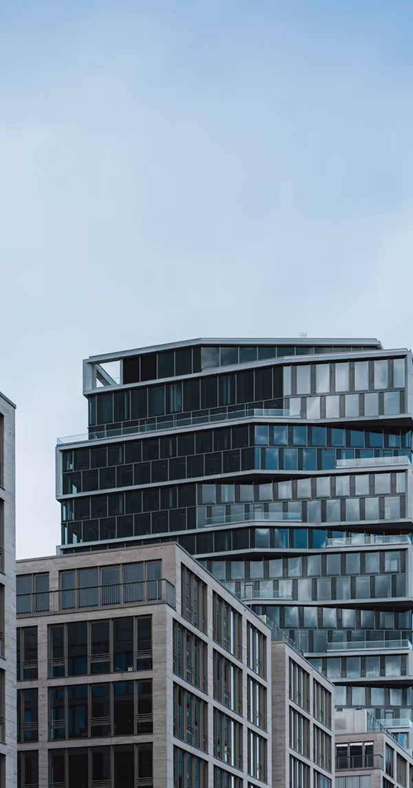 Vue d’un immeuble moderne avec des façades en verre et béton, architecture contemporaine et lignes épurées, sur fond de ciel nuageux.