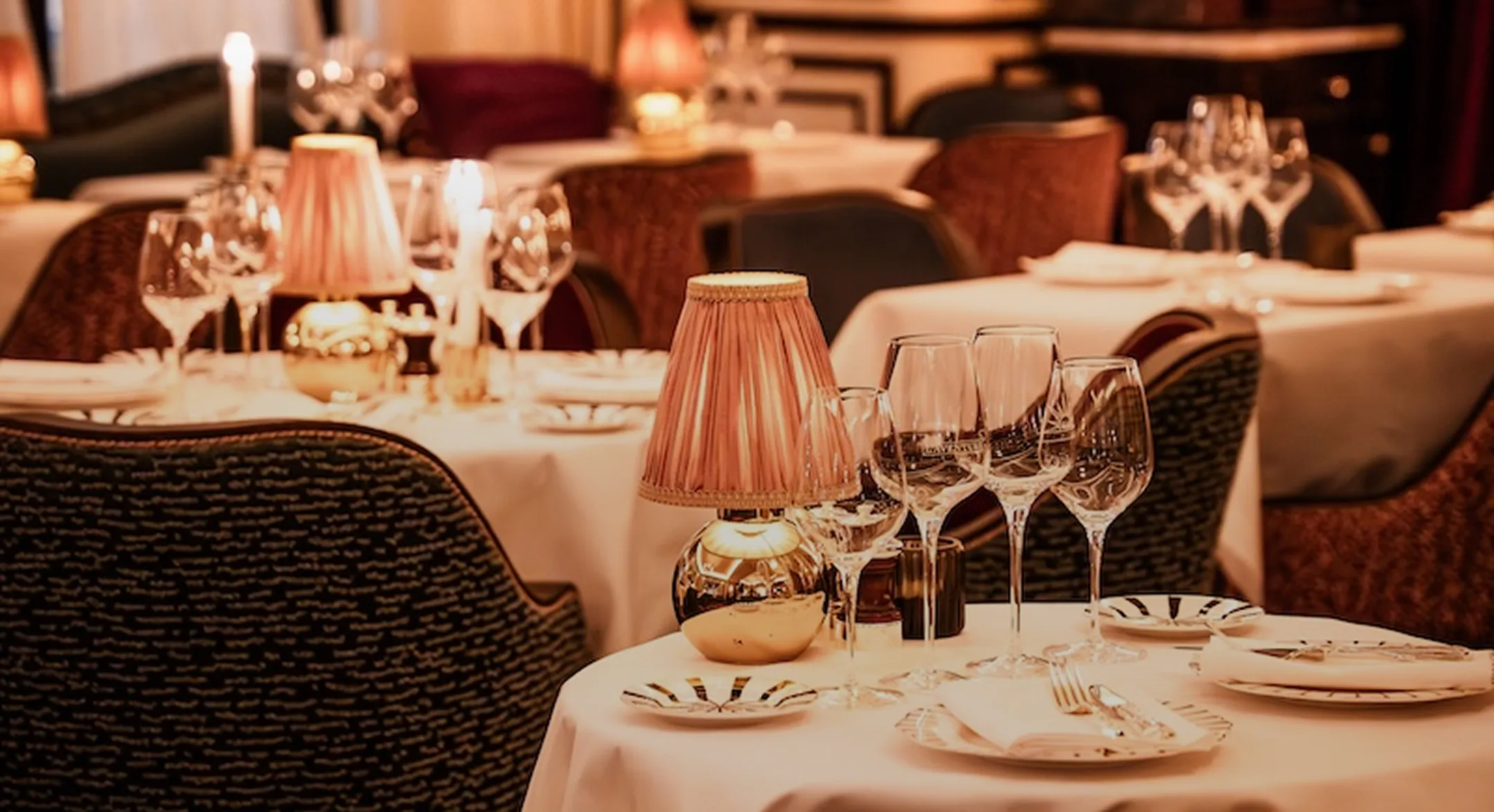 Table élégamment dressée avec nappes blanches, verres à vin, lampes à abat-jour et couverts dans un restaurant raffiné.