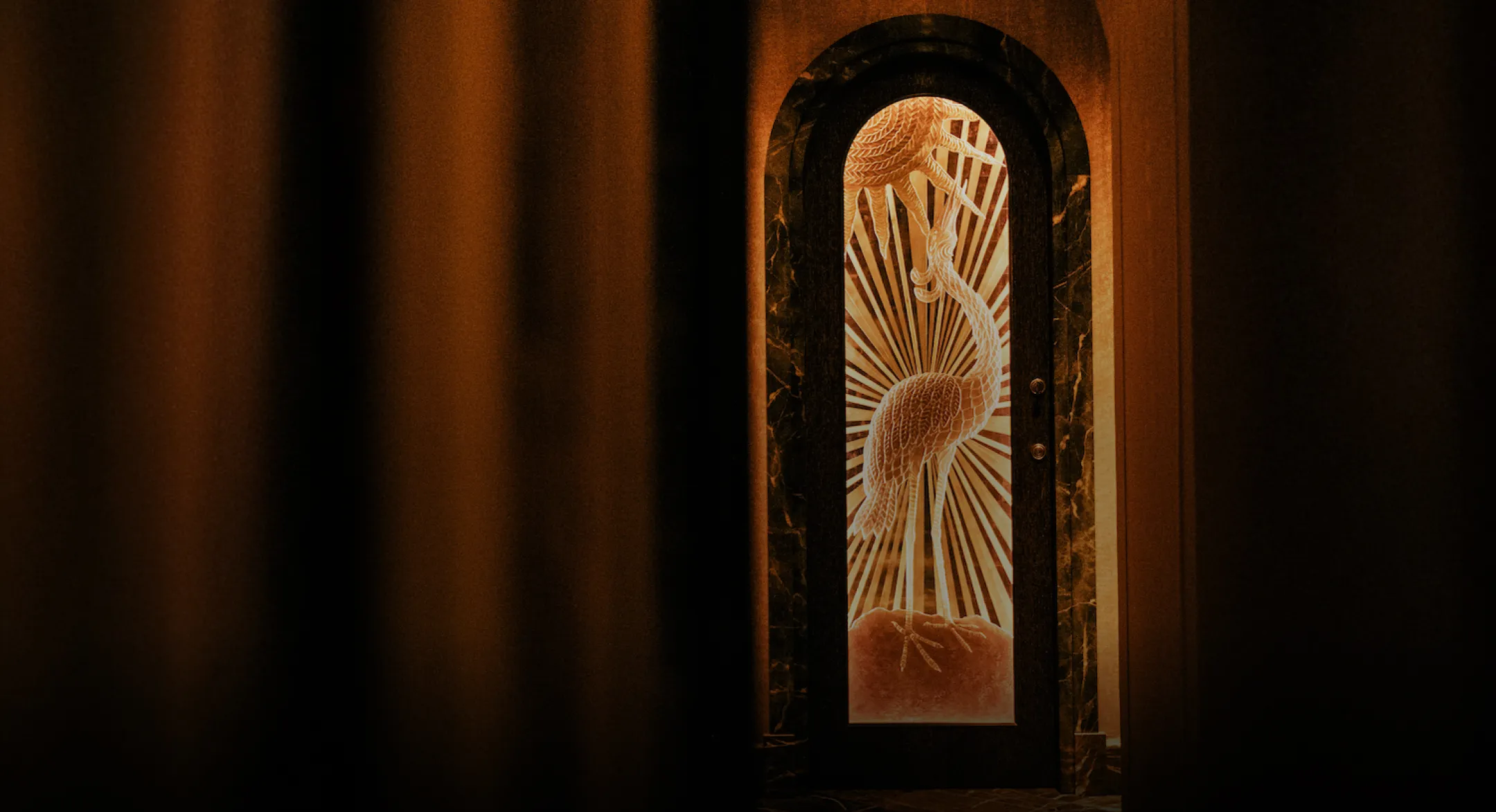 Porte en verre gravé avec une image d'un oiseau debout et des rayons derrière, entourée de murs sombres.