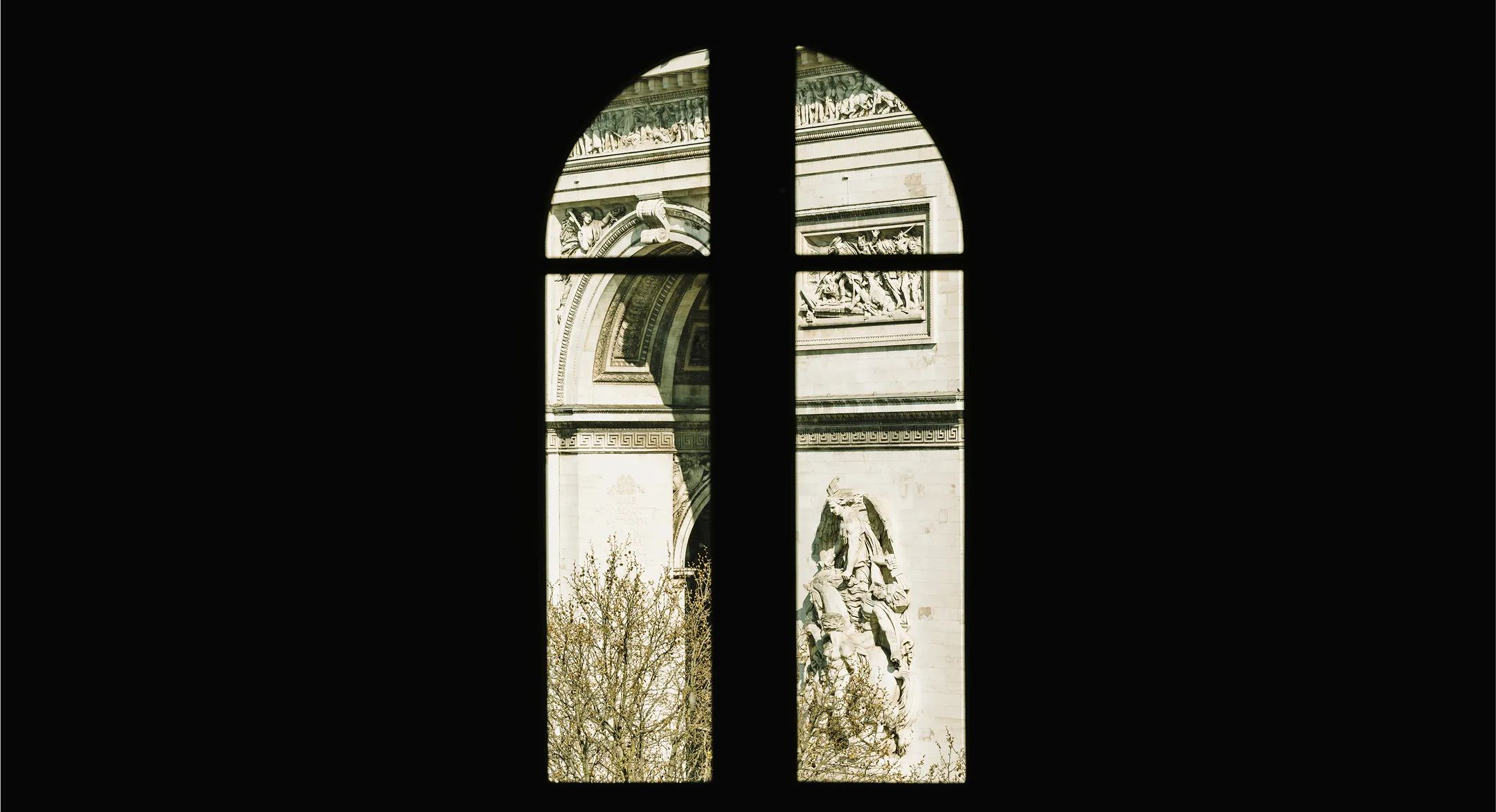 Vue partielle de l'Arc de Triomphe à travers une fenêtre en forme d'arche avec un cadre en croix.