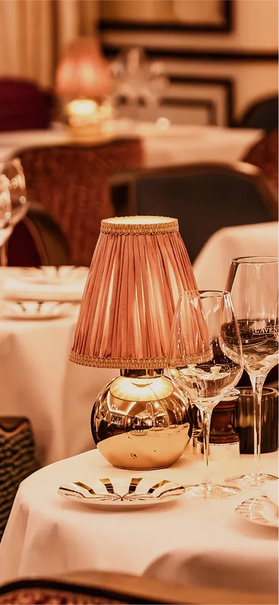 Lampe vintage avec abat-jour en tissu rose sur une table de restaurant élégamment dressée avec verres à vin et assiettes.