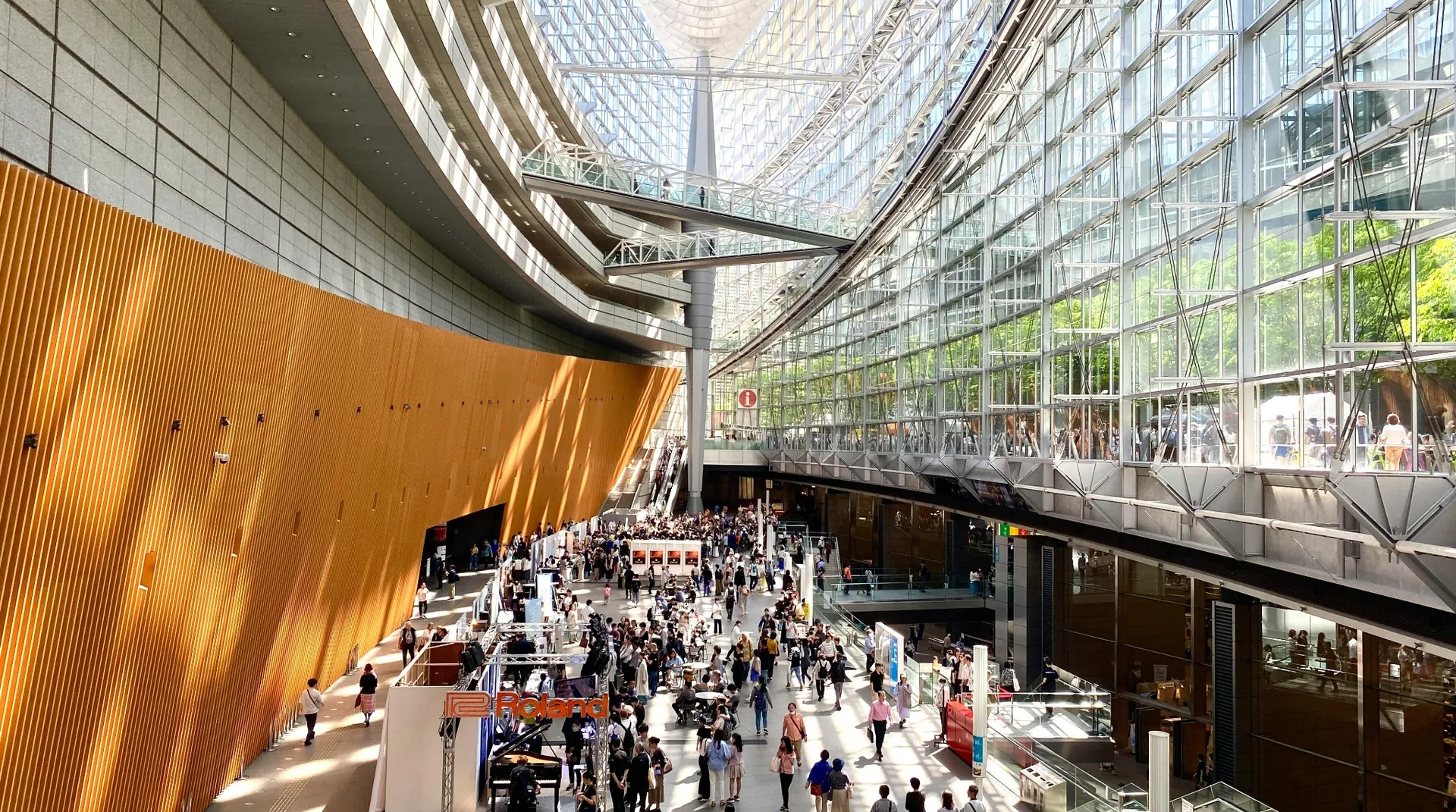 Wide view of a modern exhibition hall with multiple trade show stands, natural light, and large crowds of people walking, networking, and visiting exhibits.