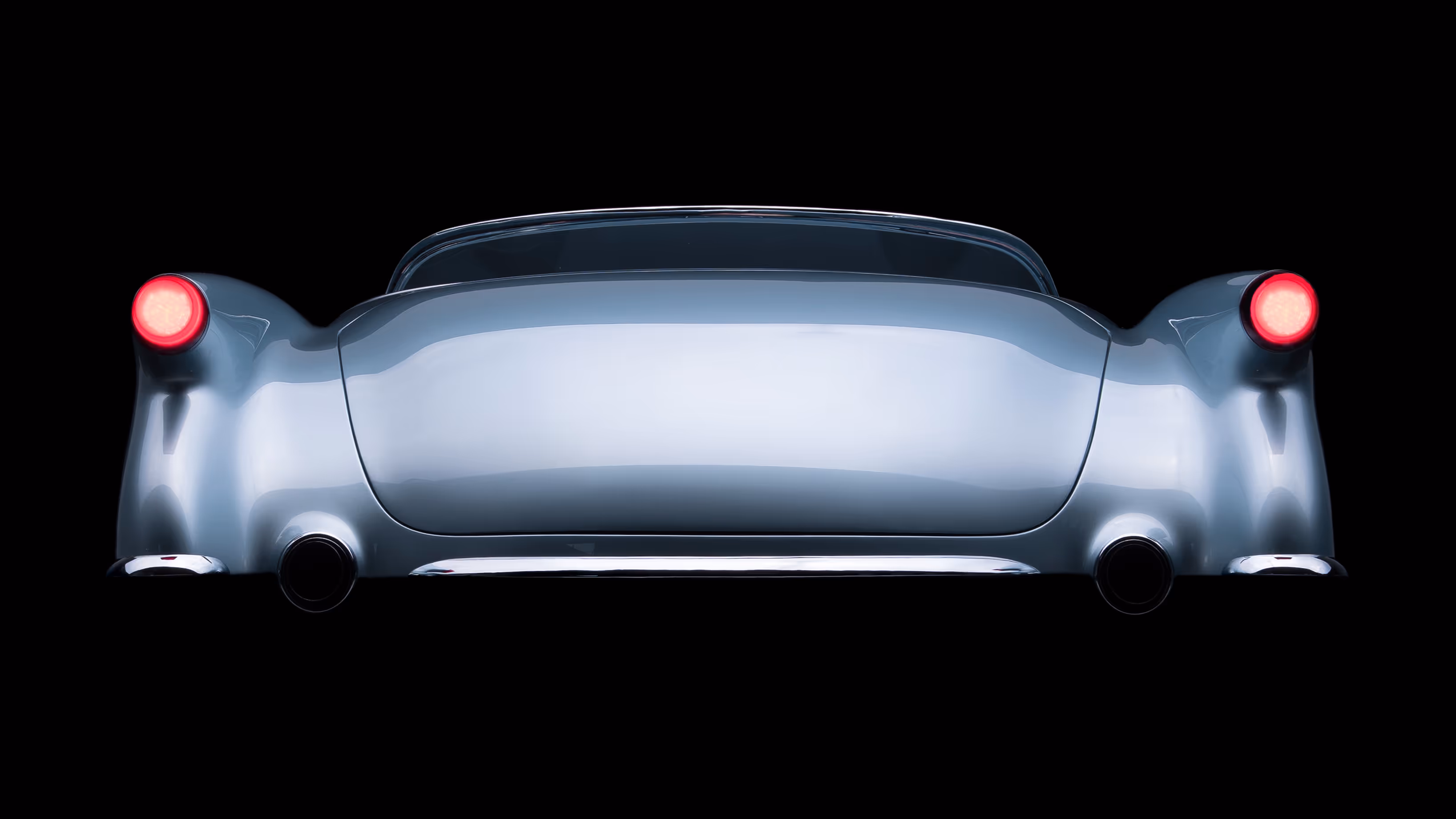 Rear view of a vintage silver convertible car with red taillights illuminated against a black background.