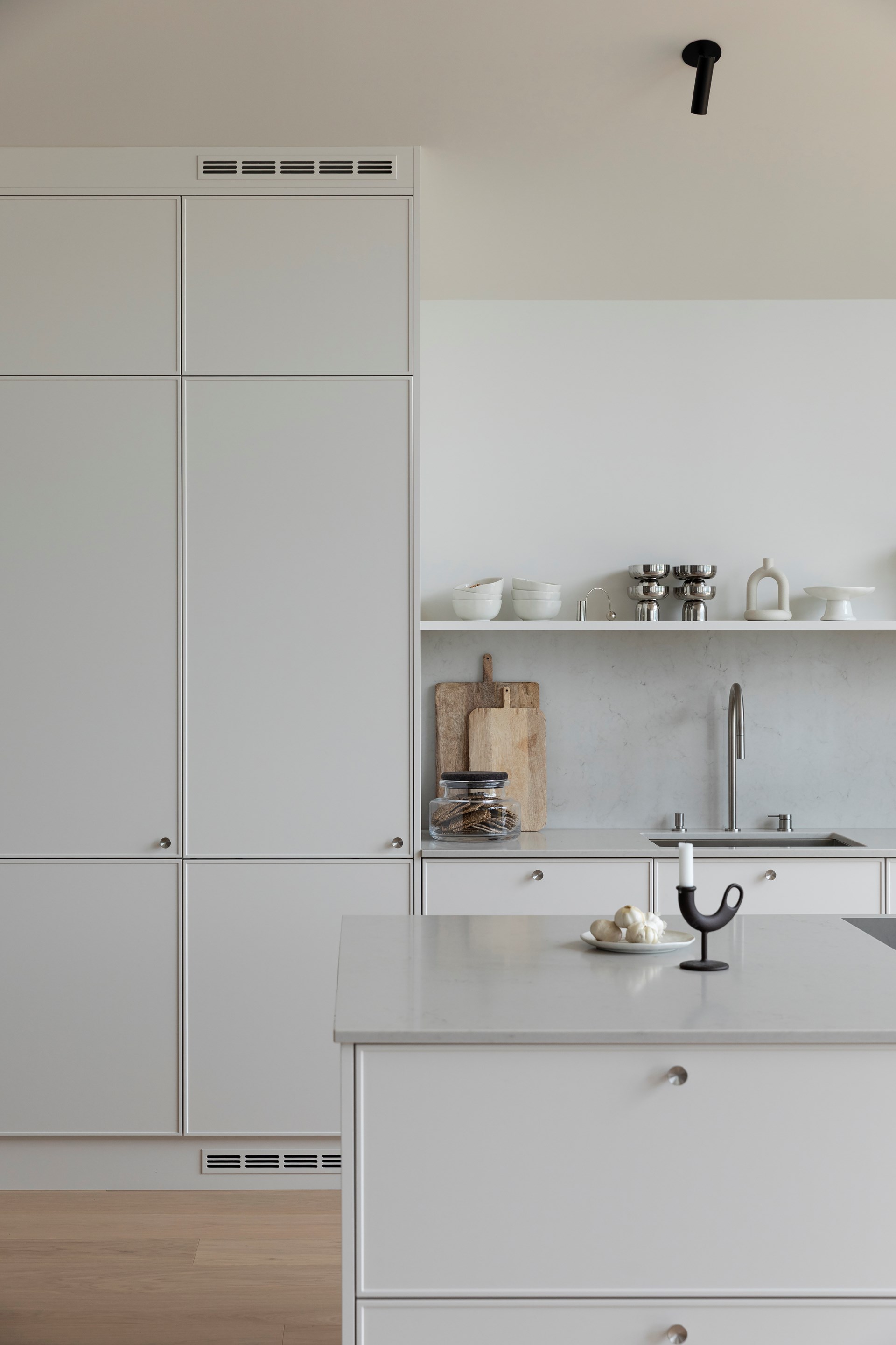 Minimalistisk hvitt kjøkken med integrerte skap, åpen hylle med hvite boller.