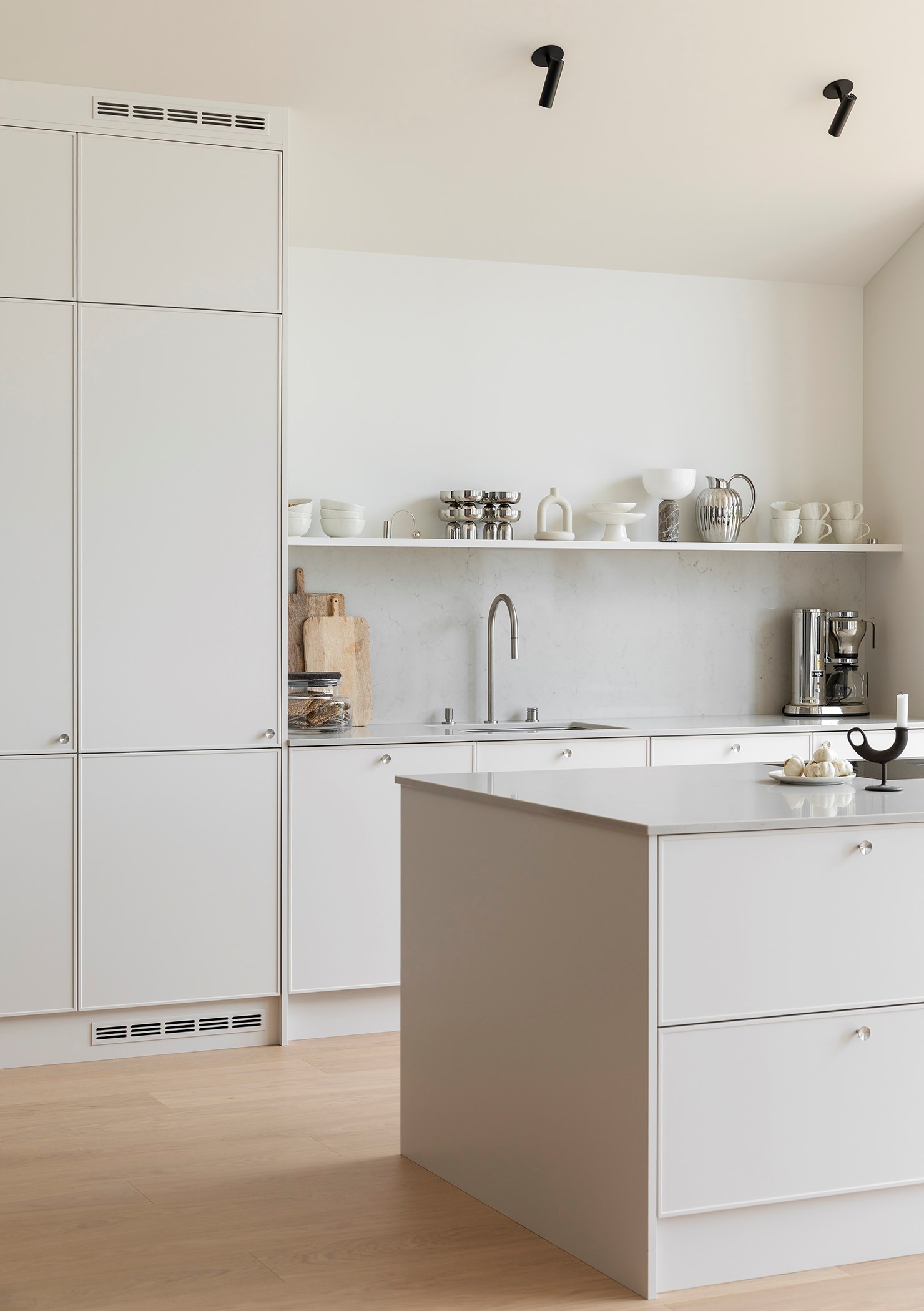 Minimalistisk hvitt kjøkken med øy, åpne hyller med servise og marmorbakvegg.