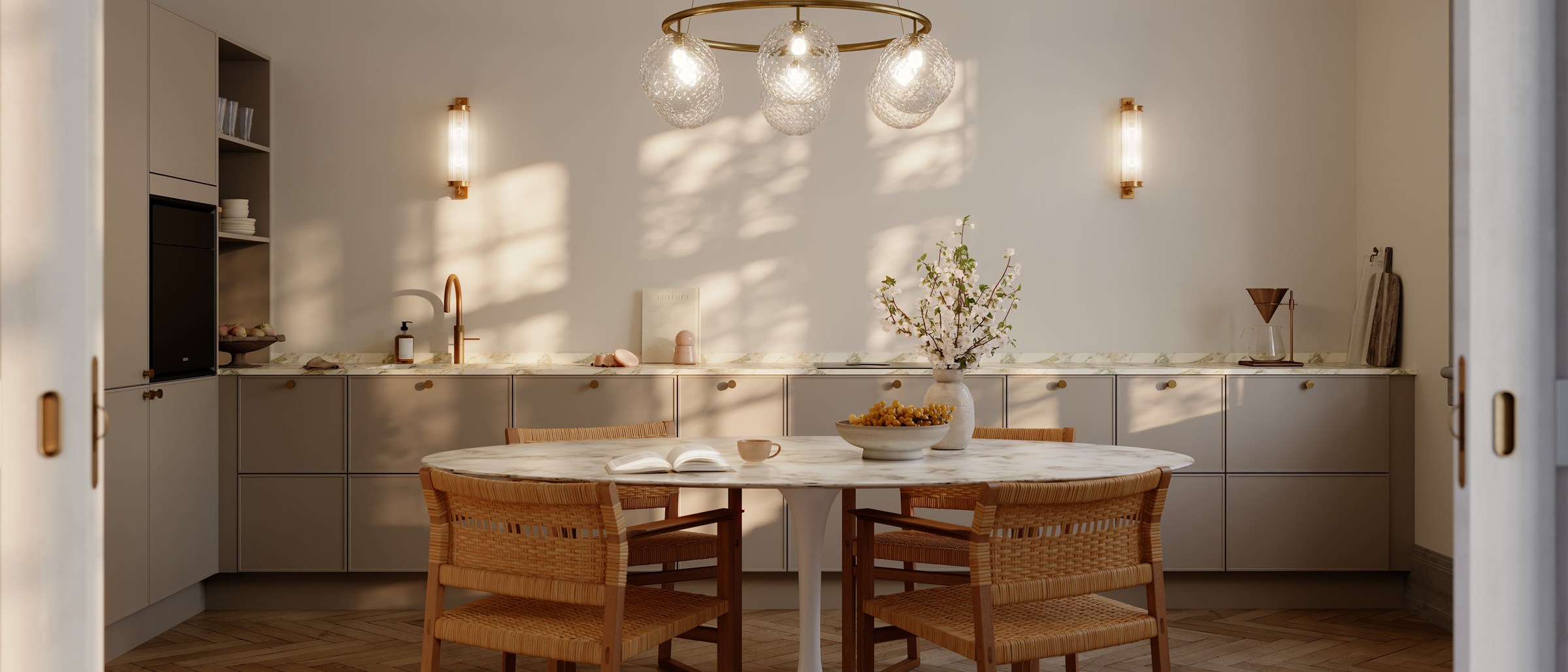 Lyst kjøkken med rundt marmorbord, rotting stoler og messinglamper. Beige skap og parkett gulv.