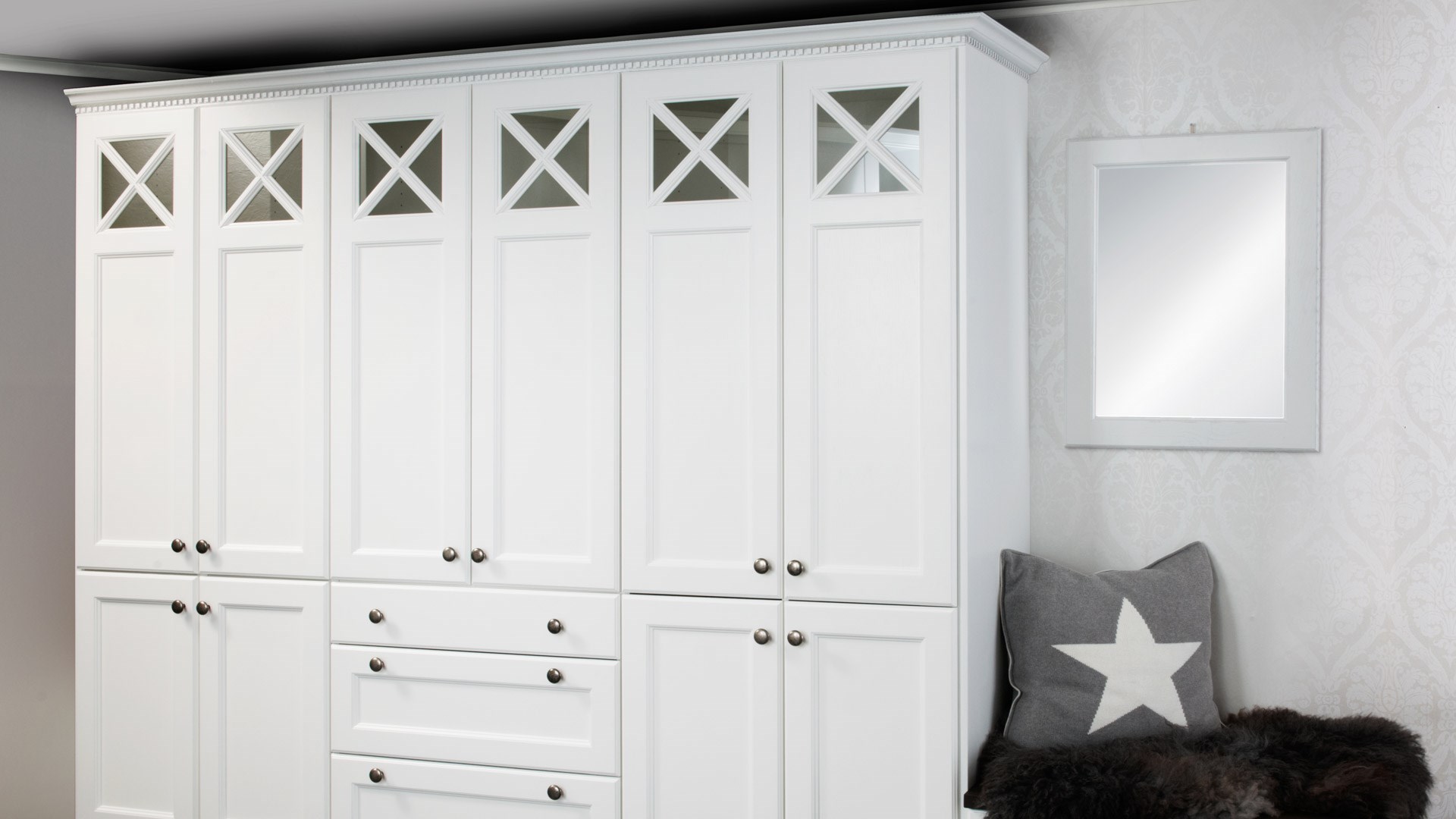 Hvit klassisk garderobe med krysspanel og glassfelt øverst, metallknotter og skuffer i midten.