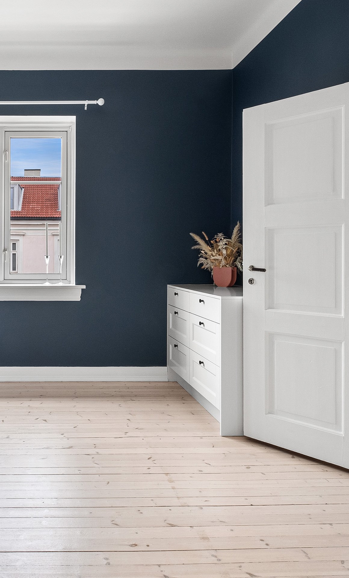 Lys entré med mørkeblå vegger, hvit kommodebenk med skuffer og tørket pampagress i terrakottapotte.
