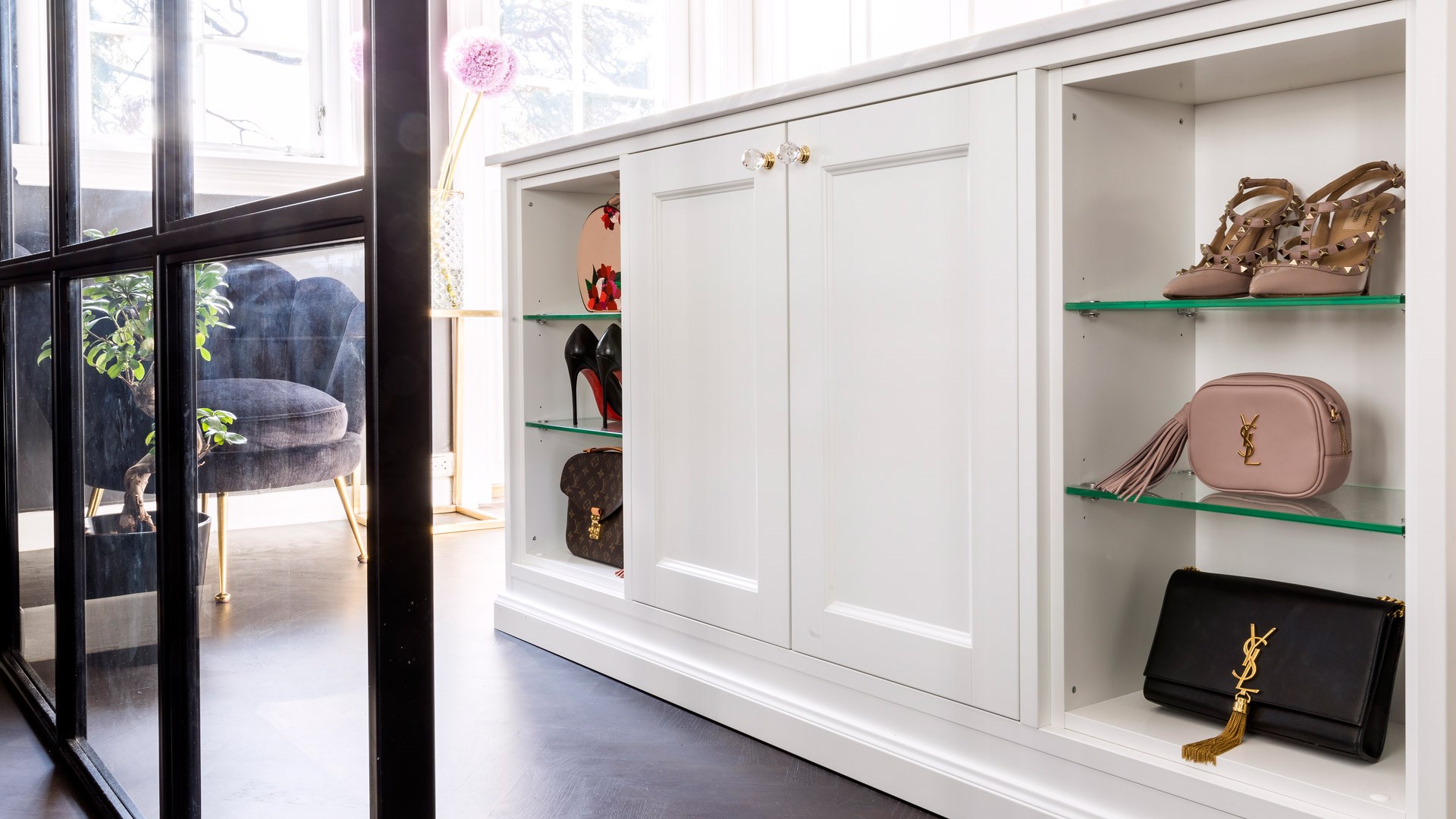 Hvit innebygd garderobe med glasshyller som viser frem luksusvesker fra YSL og Louis Vuitton, samt høyhælte sko.