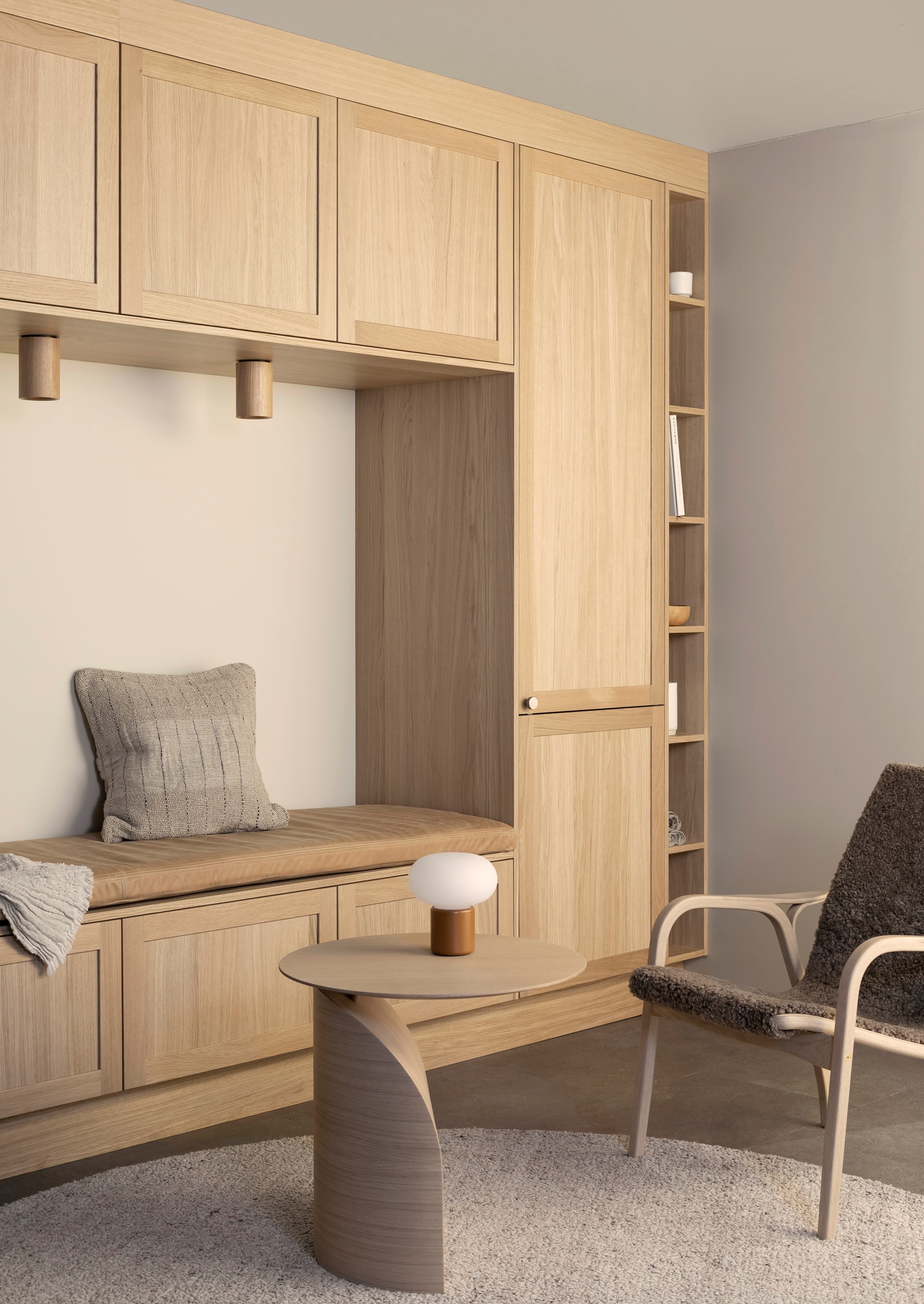 Innebygd garderobe i lyst eiketre med benk, overskap og hyller. Liten rundt bord og lenestol i forgrunnen.
