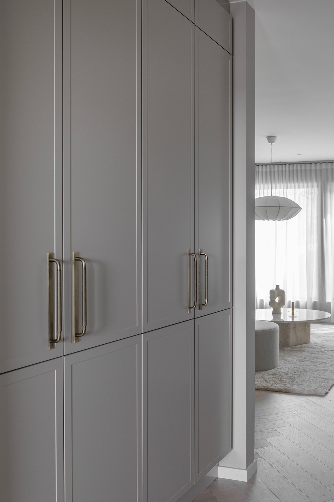 Innebygd grå garderobe med messinghåndtak, med utsikt til stue med rundt marmorbord og pendellampe.
