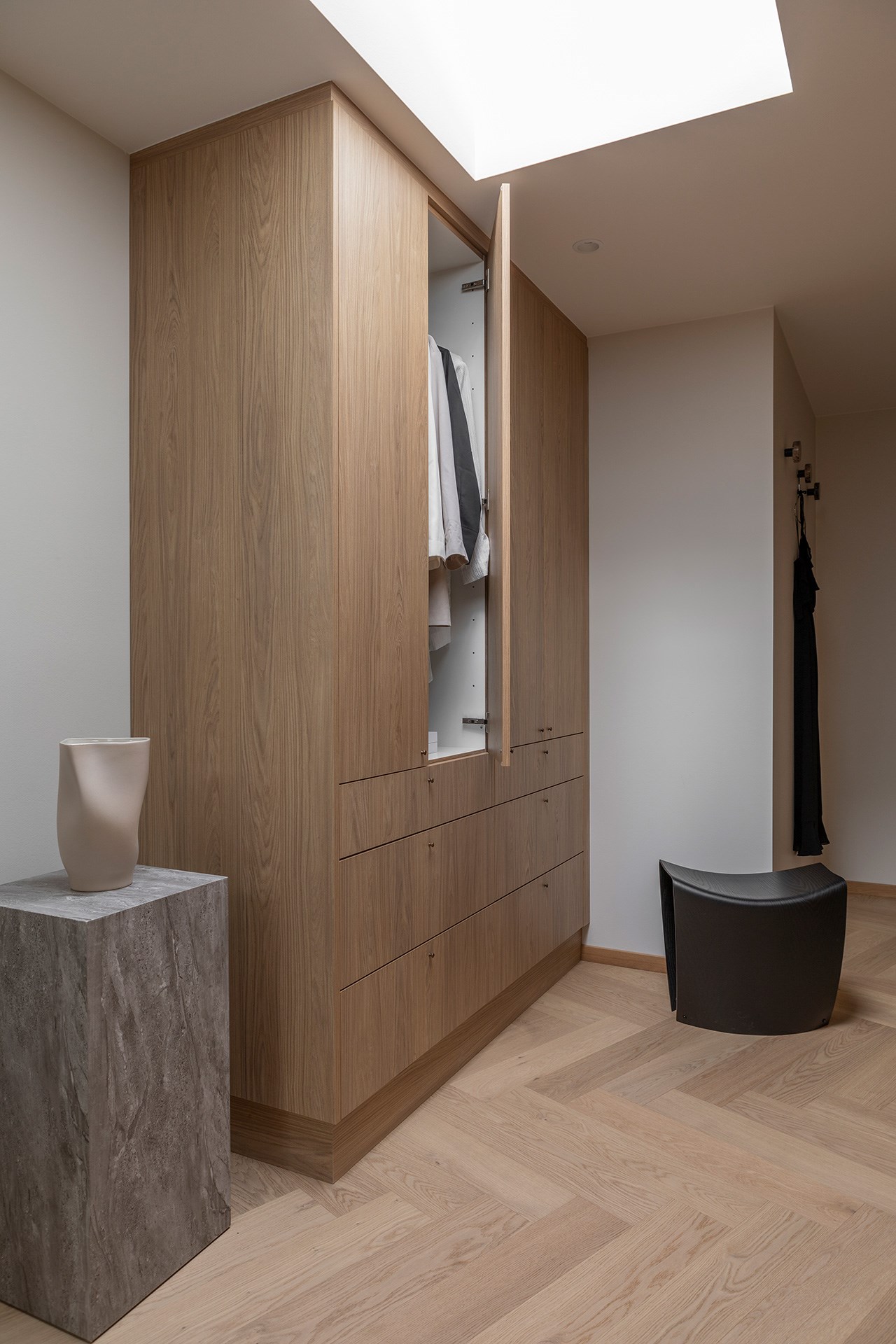 Innebygd eikeskapsgarderobe med åpen dør, skuffer og skråtak med ovenlys i moderne interiør.