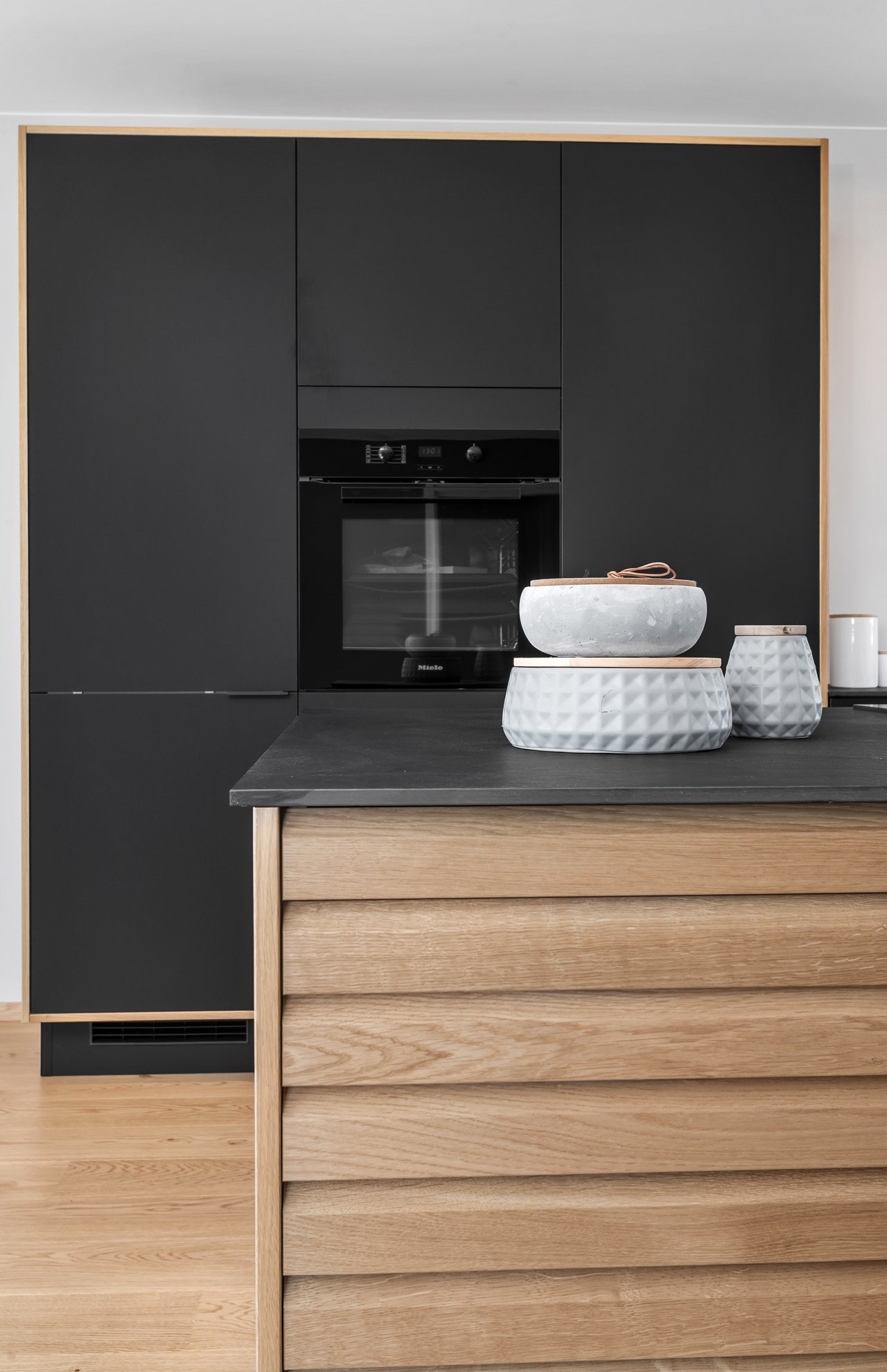 Moderne kjøkken med mattsvarte skap, innebygd Miele-ovn og en treøy med mørk benkeplate.