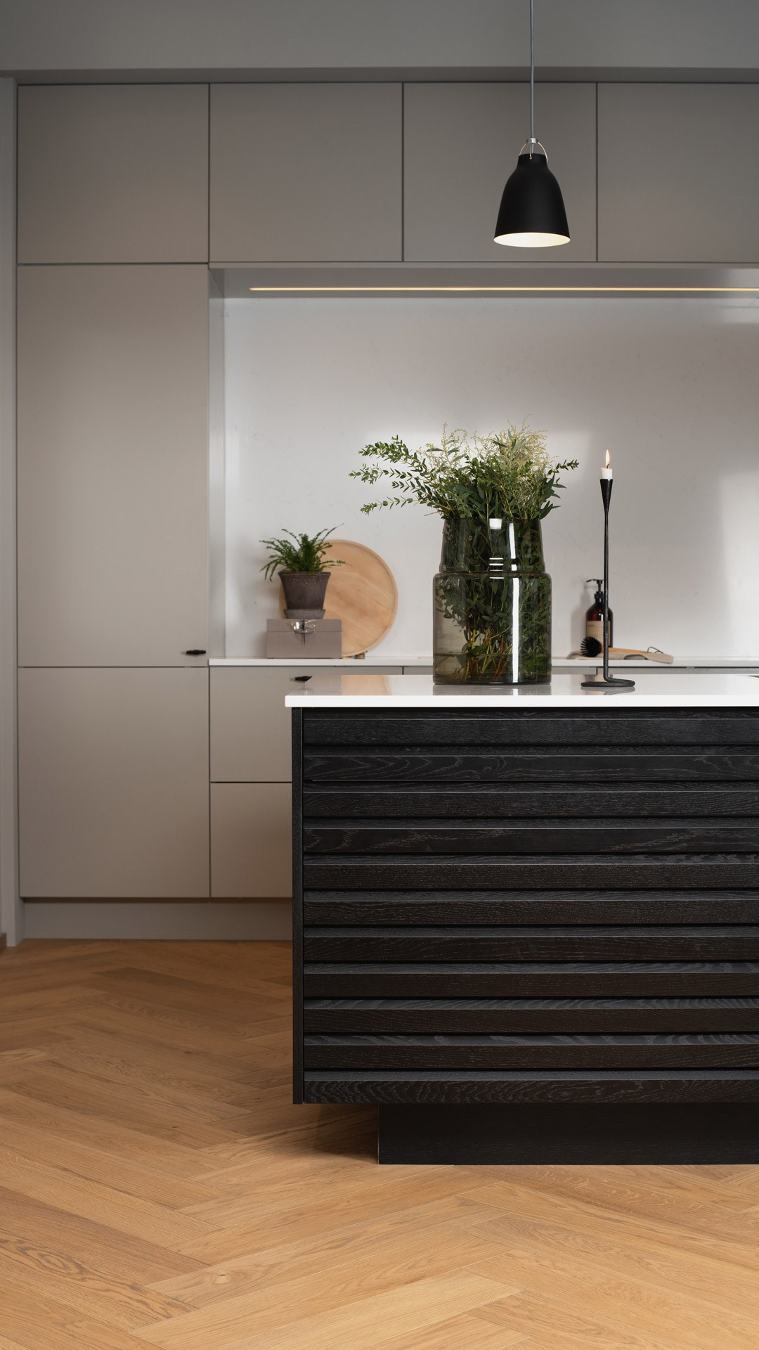 Moderne kjøkken med sort treøy, grå skap, parkettgulv og grønn glassvase med planter.