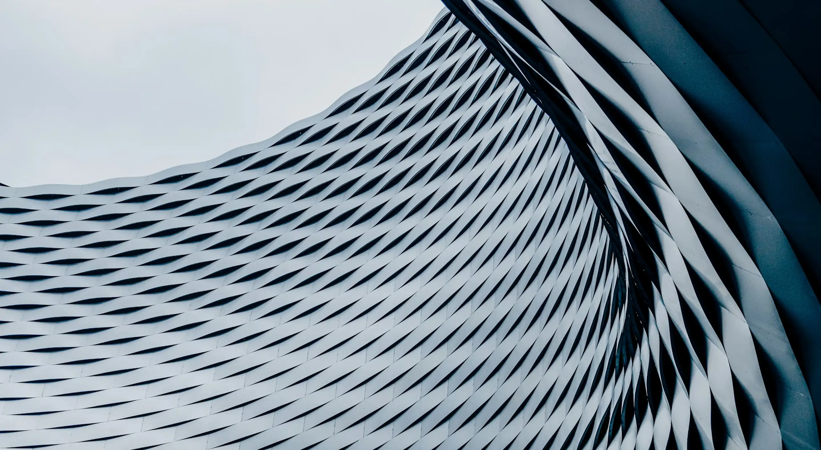 Curved architectural facade with a repetitive diamond-shaped pattern in shades of gray and blue.