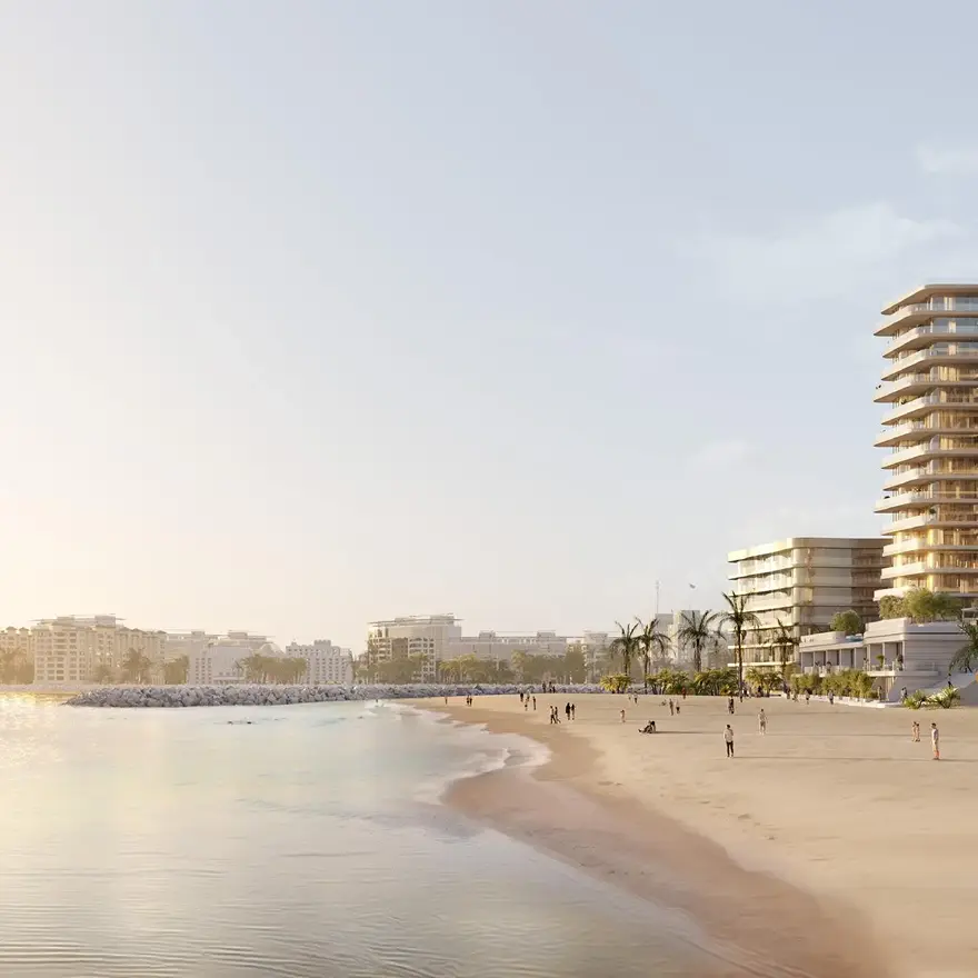 Sunny beach with calm ocean waves, people walking and relaxing on the sand, and modern buildings with palm trees in the background. Invest in Ras Al Khaimah Luxury Real Estate