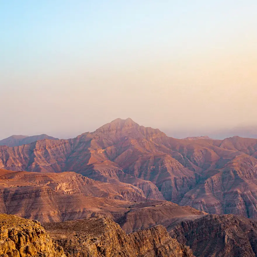 Range of brown rocky mountains under a clear sky during sunset. Invest in Ras Al Khaimah Luxury Real Estate