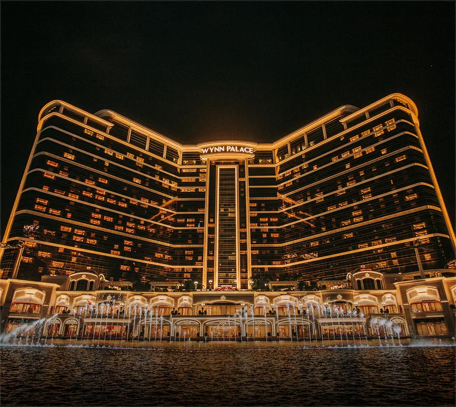 Wynn Palace hotel illuminated with golden lights and fountains in front at night.