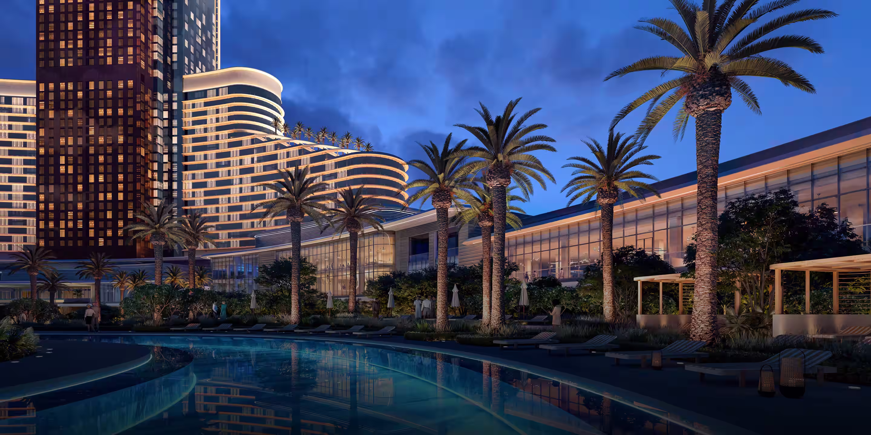 Modern high-rise buildings and curved architecture illuminated at dusk behind palm trees and a calm pool.