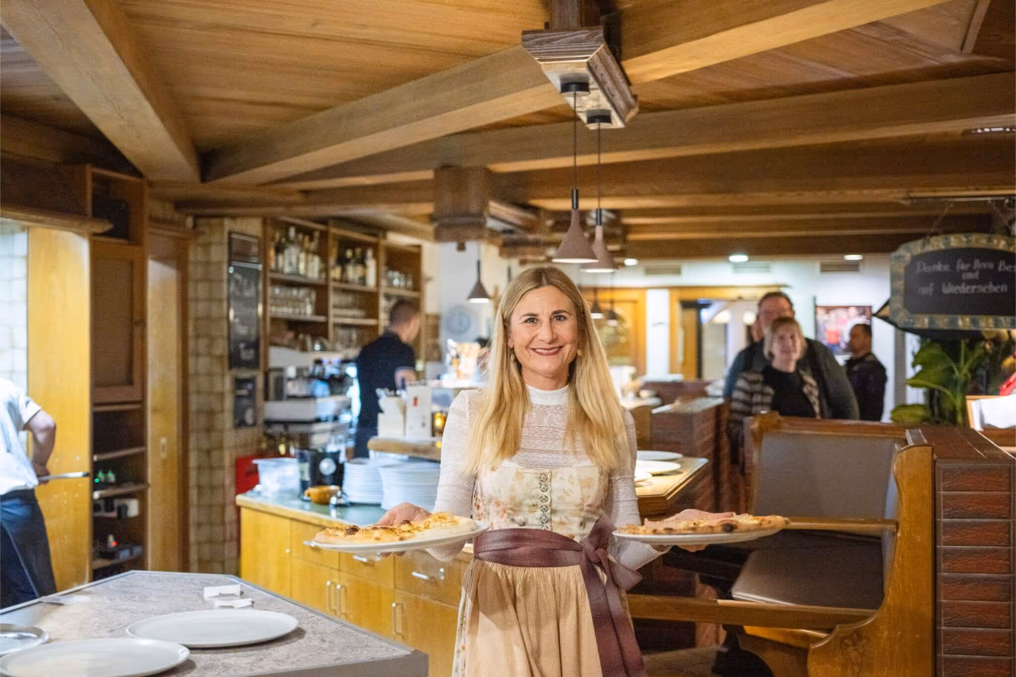 Lächelnde Kellnerin trägt in einem rustikalen Restaurant zwei Pizzen auf Tellern.